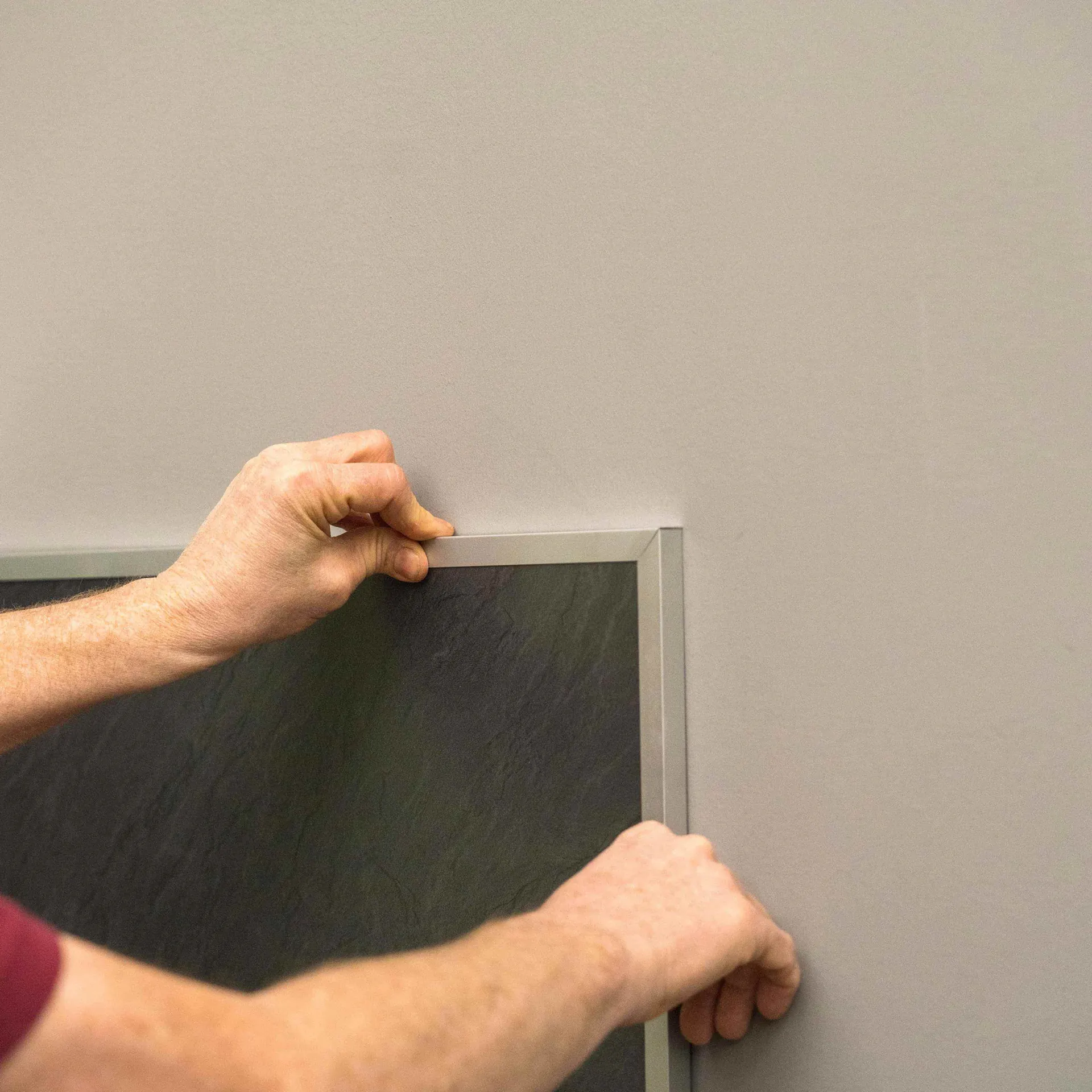 Ein Mann bringt eine Aluminiumleiste an einer Küchenrückwand an.