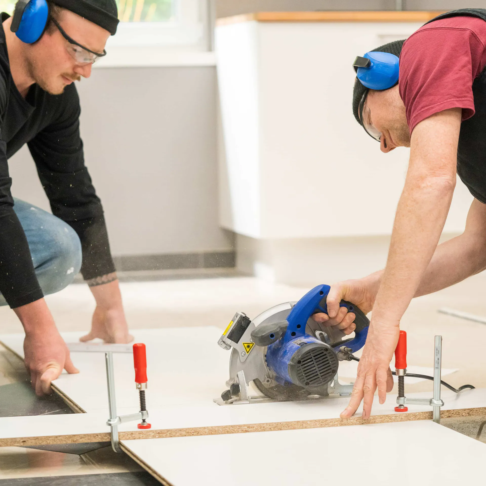 Zwei Handwerker schneiden eine Küchenrückwand zu.