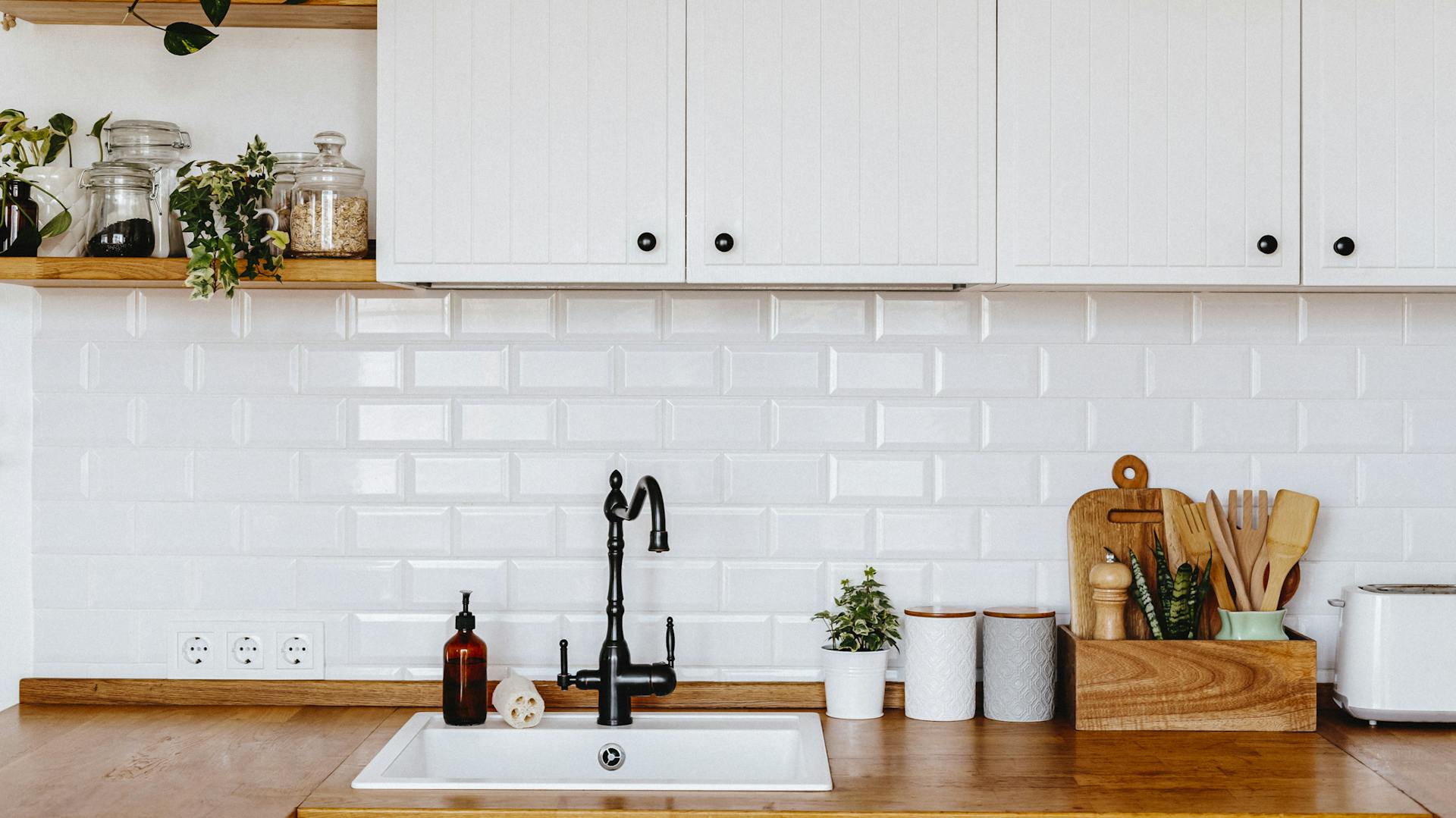 Holzarbeitsfläche mit eingelassenem weißem Keramikwaschbecken und schwarzem Wasserhahn. Darüber weiße Küchenschränke.