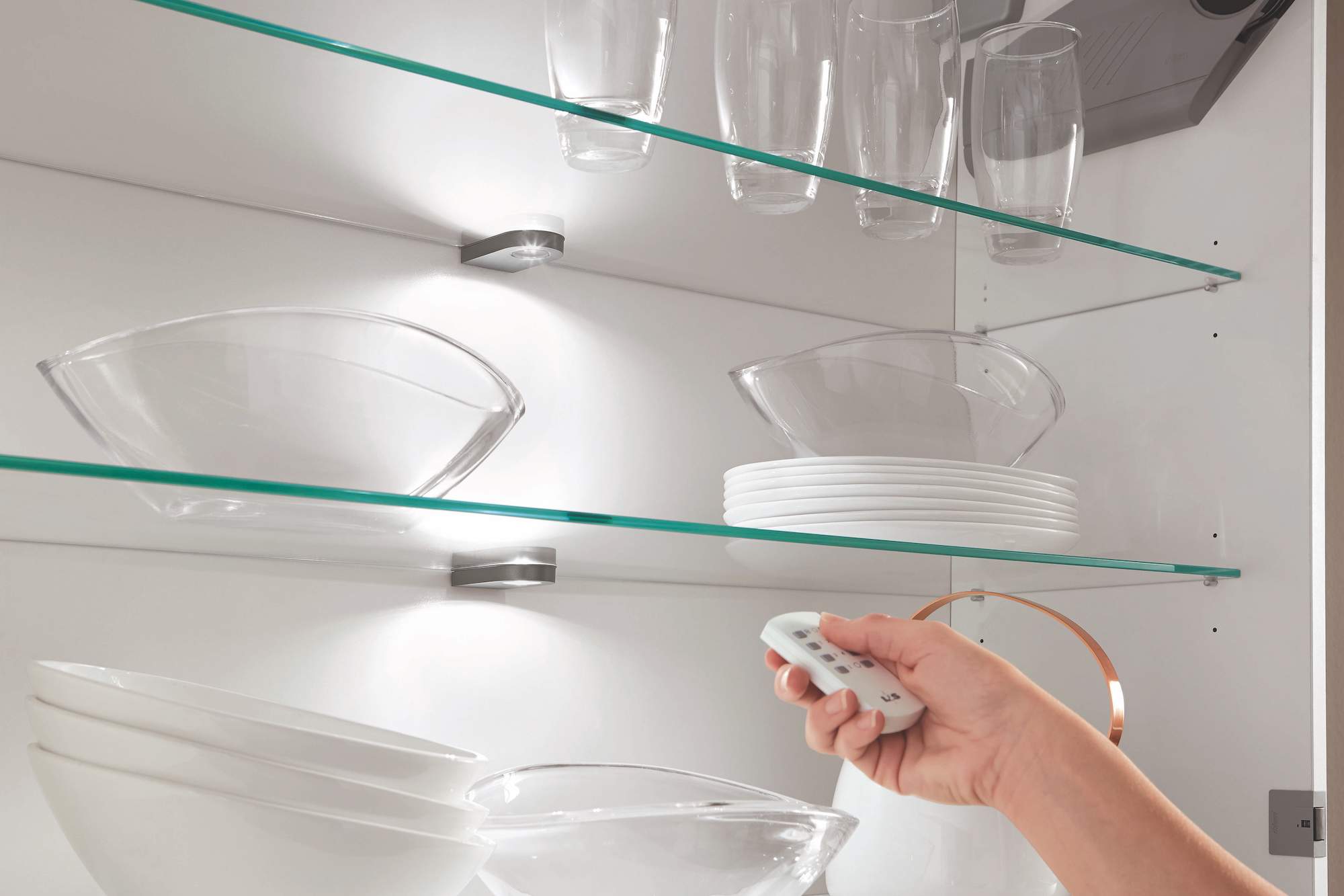 Person steuert Beleuchtung in Küchenregal mit Fernbedienung aus Smart Home.