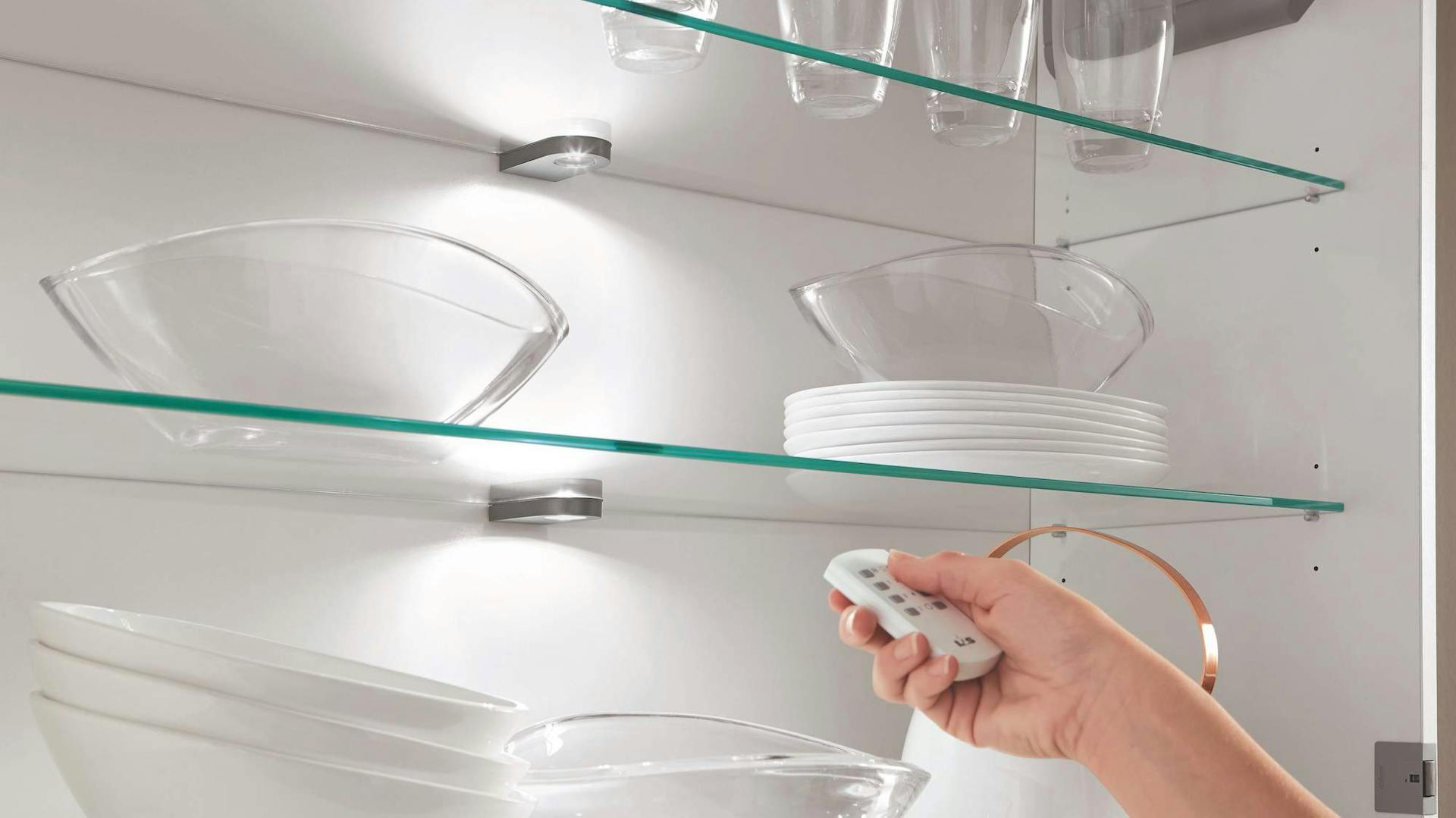 Person steuert Beleuchtung in Küchenregal mit Fernbedienung aus Smart Home.