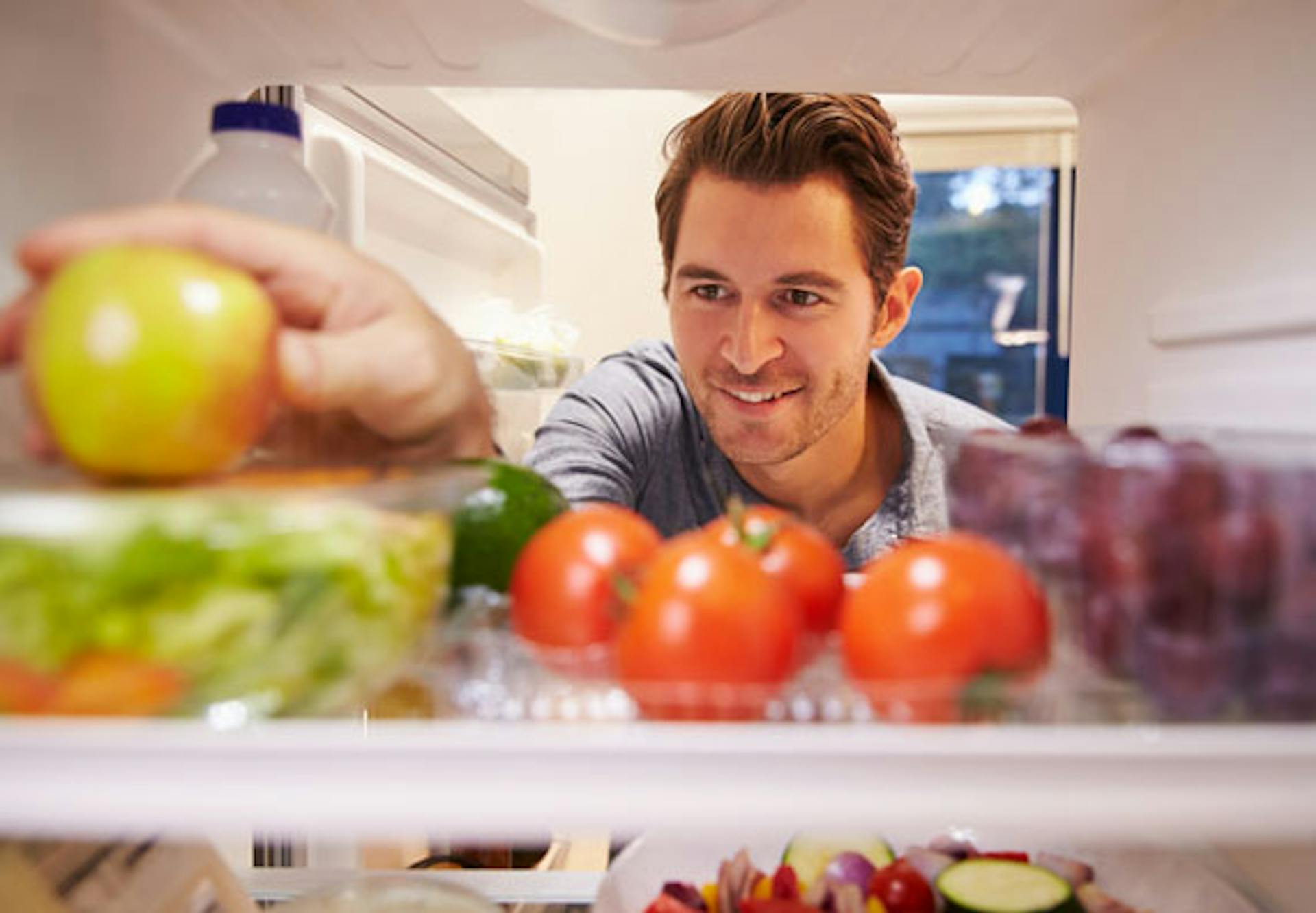 Un uomo guarda nel frigorifero e prende una mela fresca