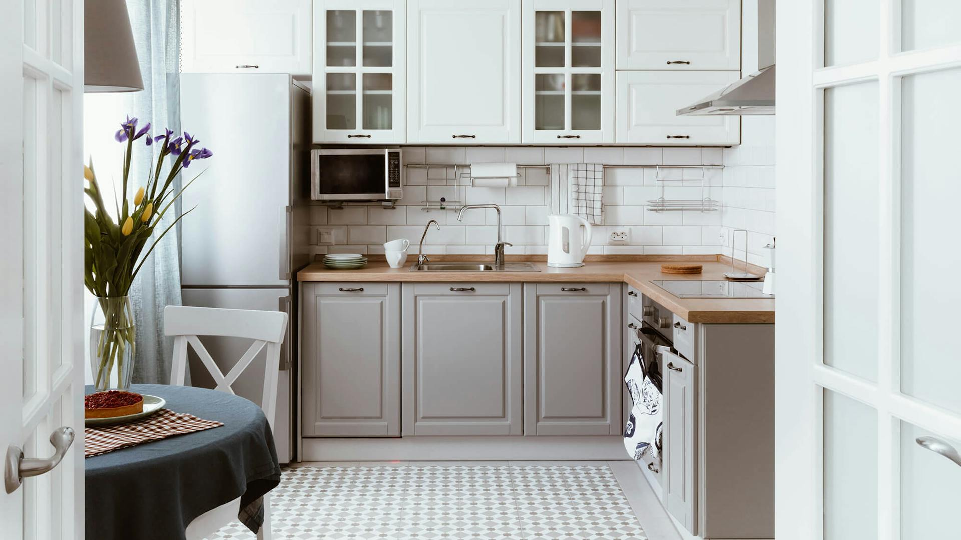 Graue Küche in L-Form. Links außen steht ein Tisch mit einer Blumenvase und Kuchen.