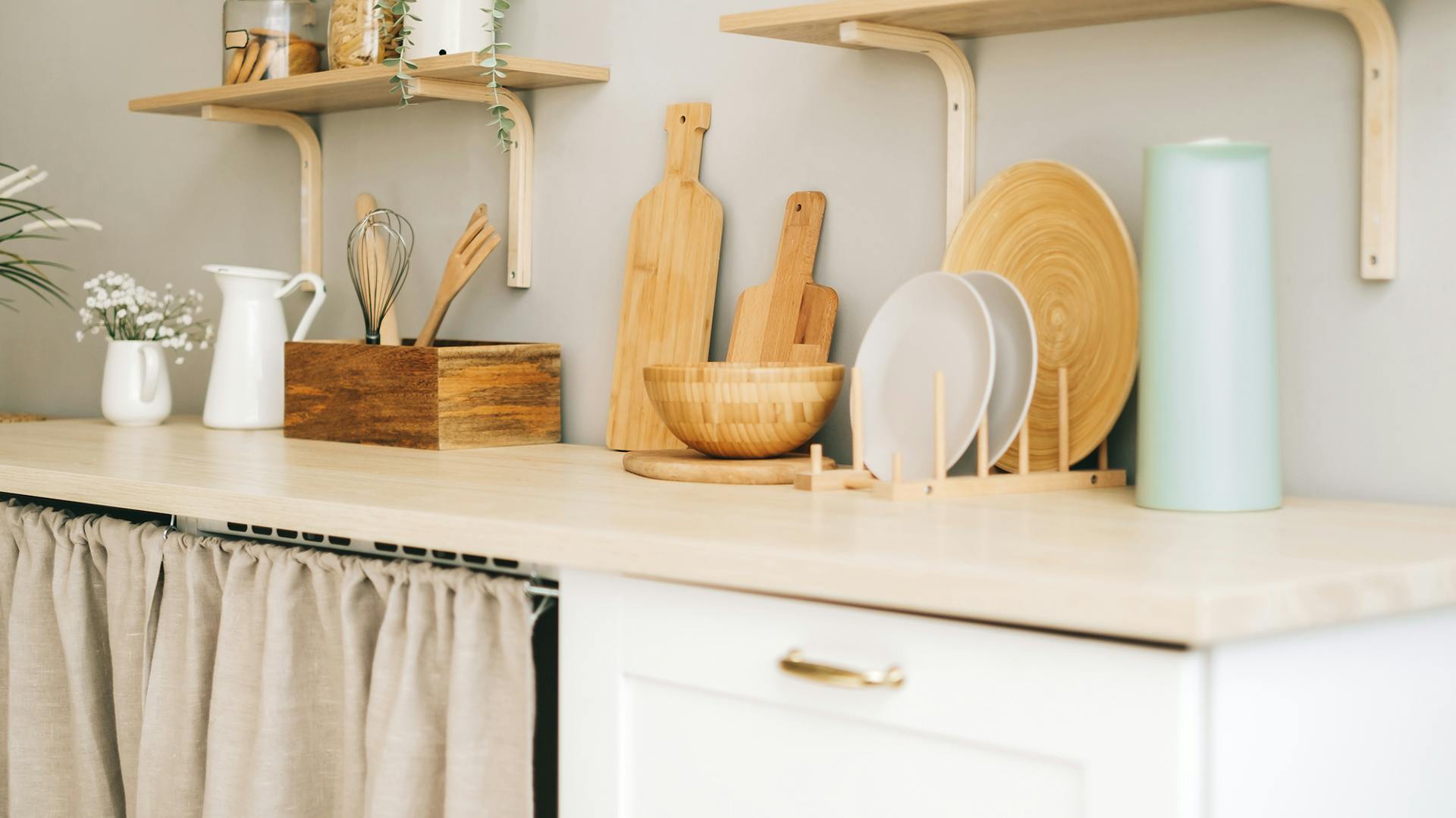 Holzbretter und helle Teller auf einer Küchenarbeitsfläche dekorativ vor einer grauen Wand.