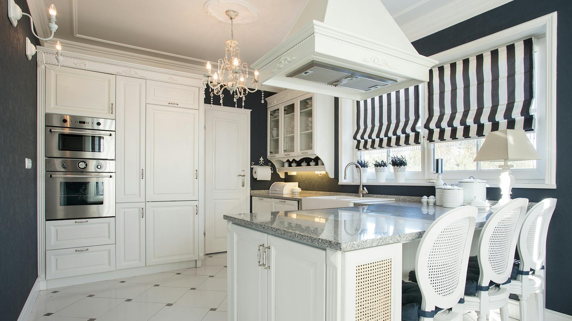 Moderne Landhausküche in weiß mit Kücheninsel und drei Stühlen vor dunkelgrauer Wand.