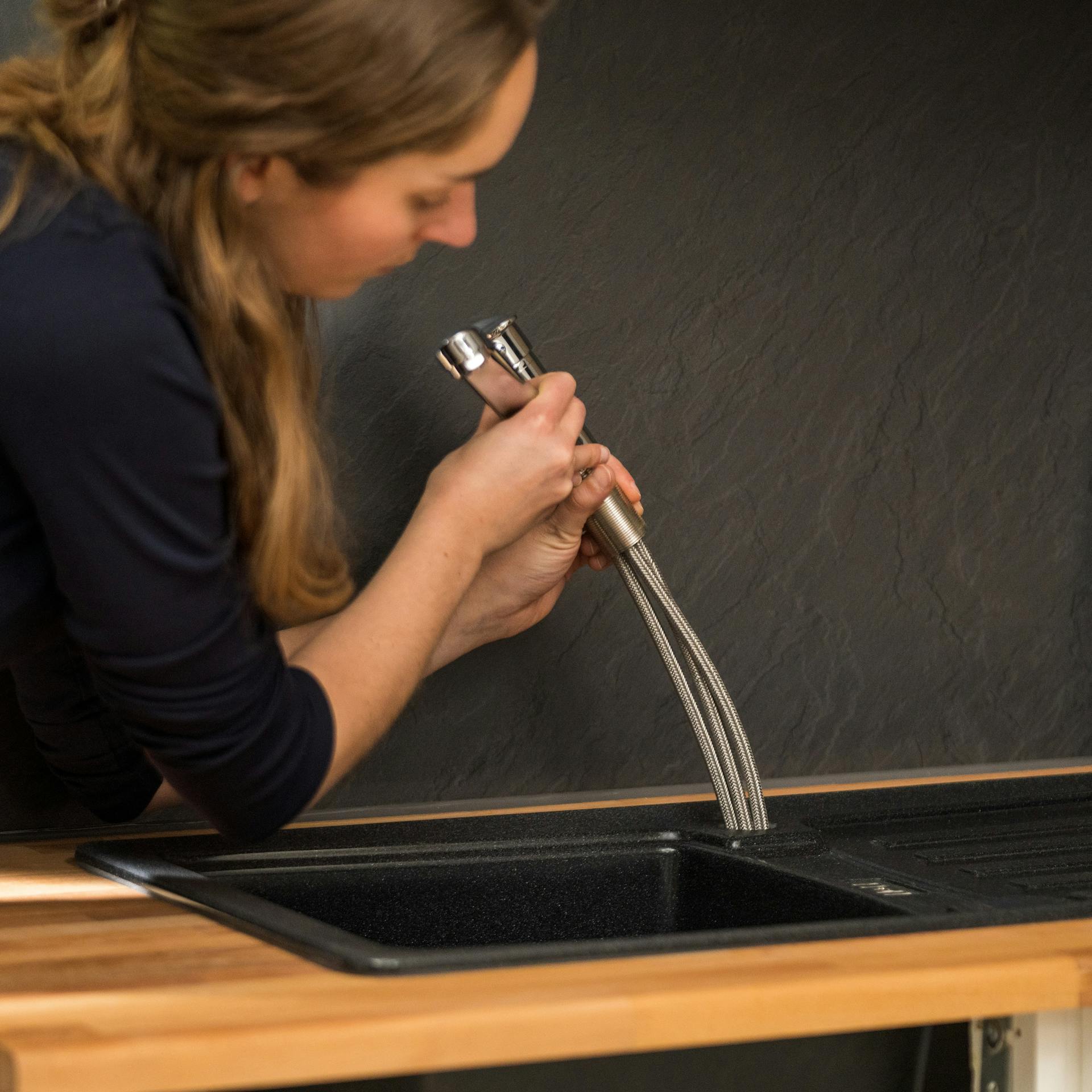 Egy barkácsoló nő eltávolítja a csaptelepet felülről a mosdókagylóból.