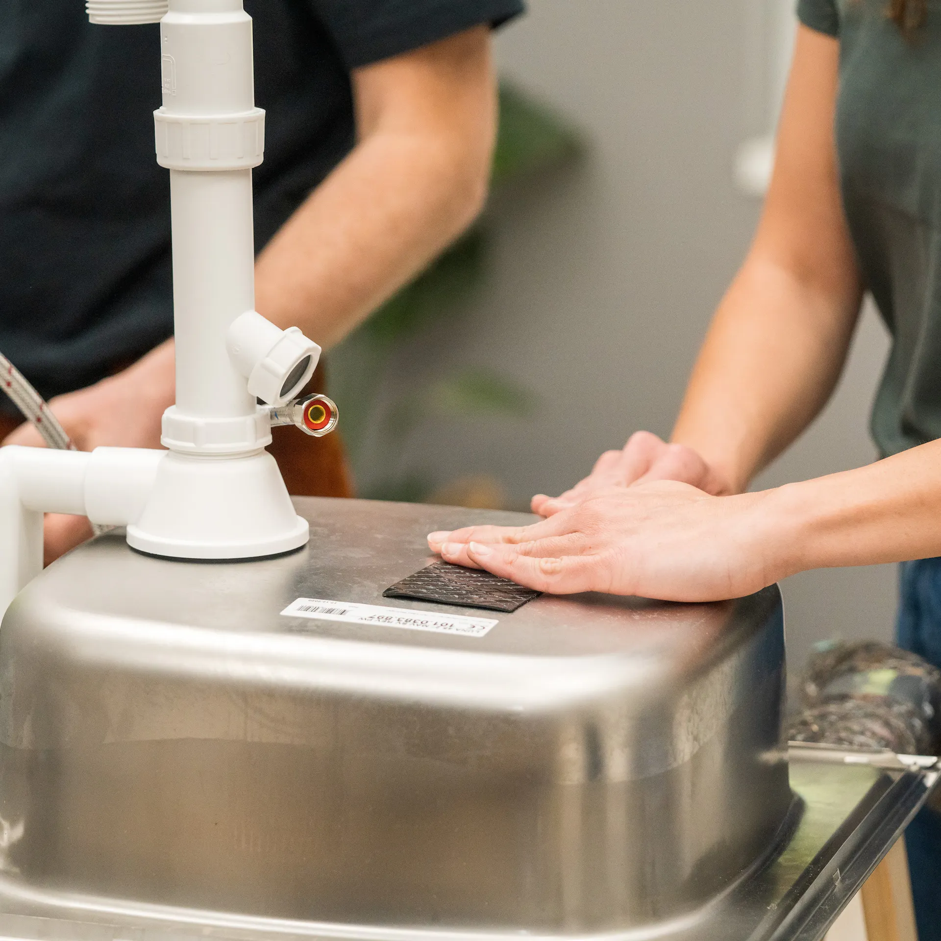 Zwei Handwerker verkleben Schallschutzband unter der Spüle.