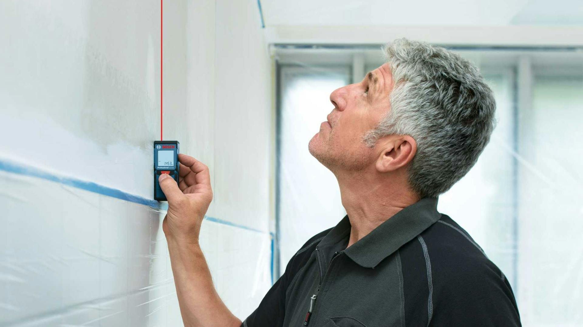 Mann hält Messgerät an Wand