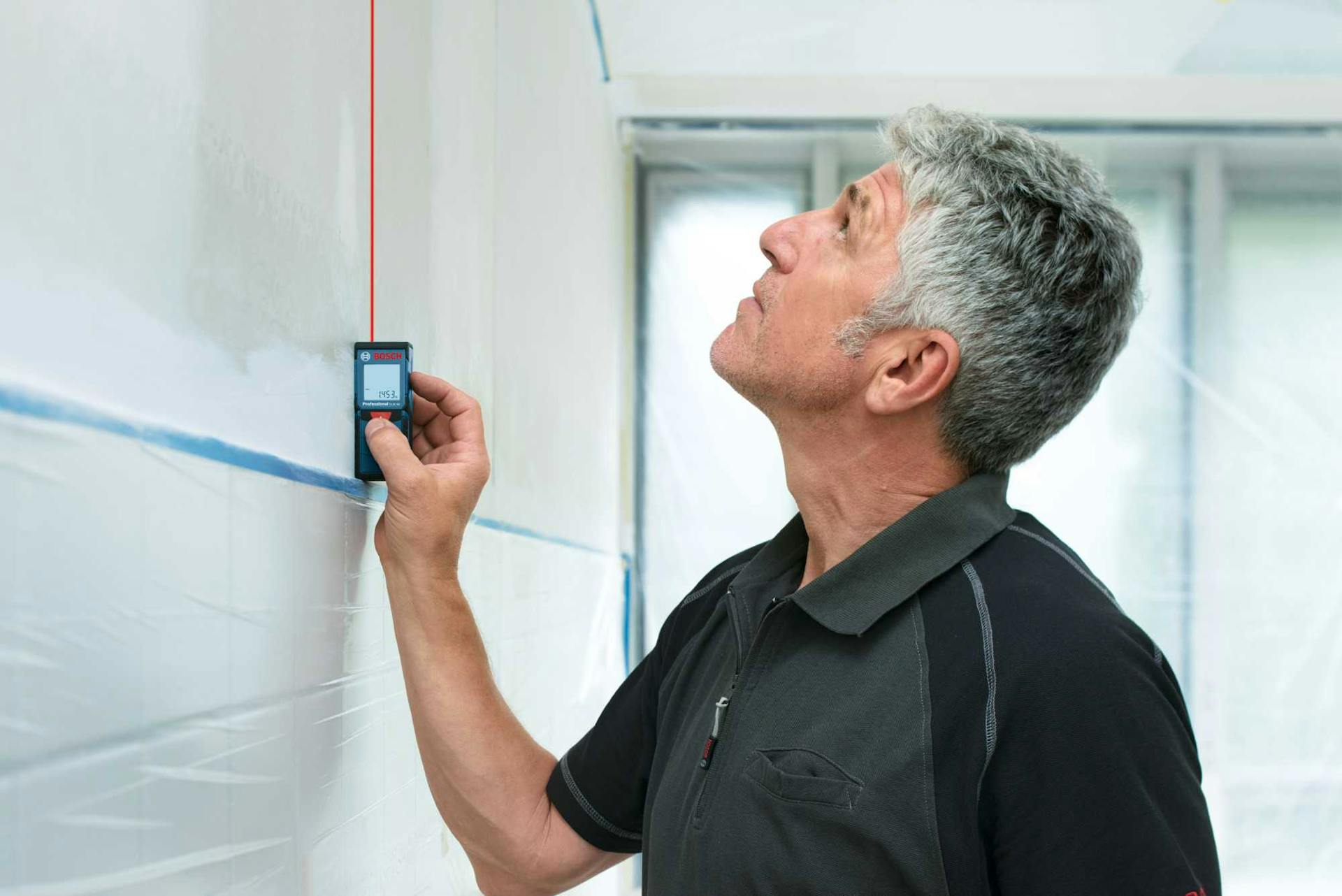 Mann misst Höhe der Küchenrückwand mit Laser-Messgerät.