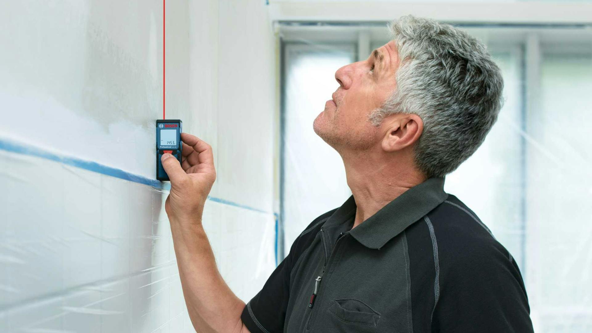 Muž meria výšku zadnej steny v kuchyni laserovým meračom.