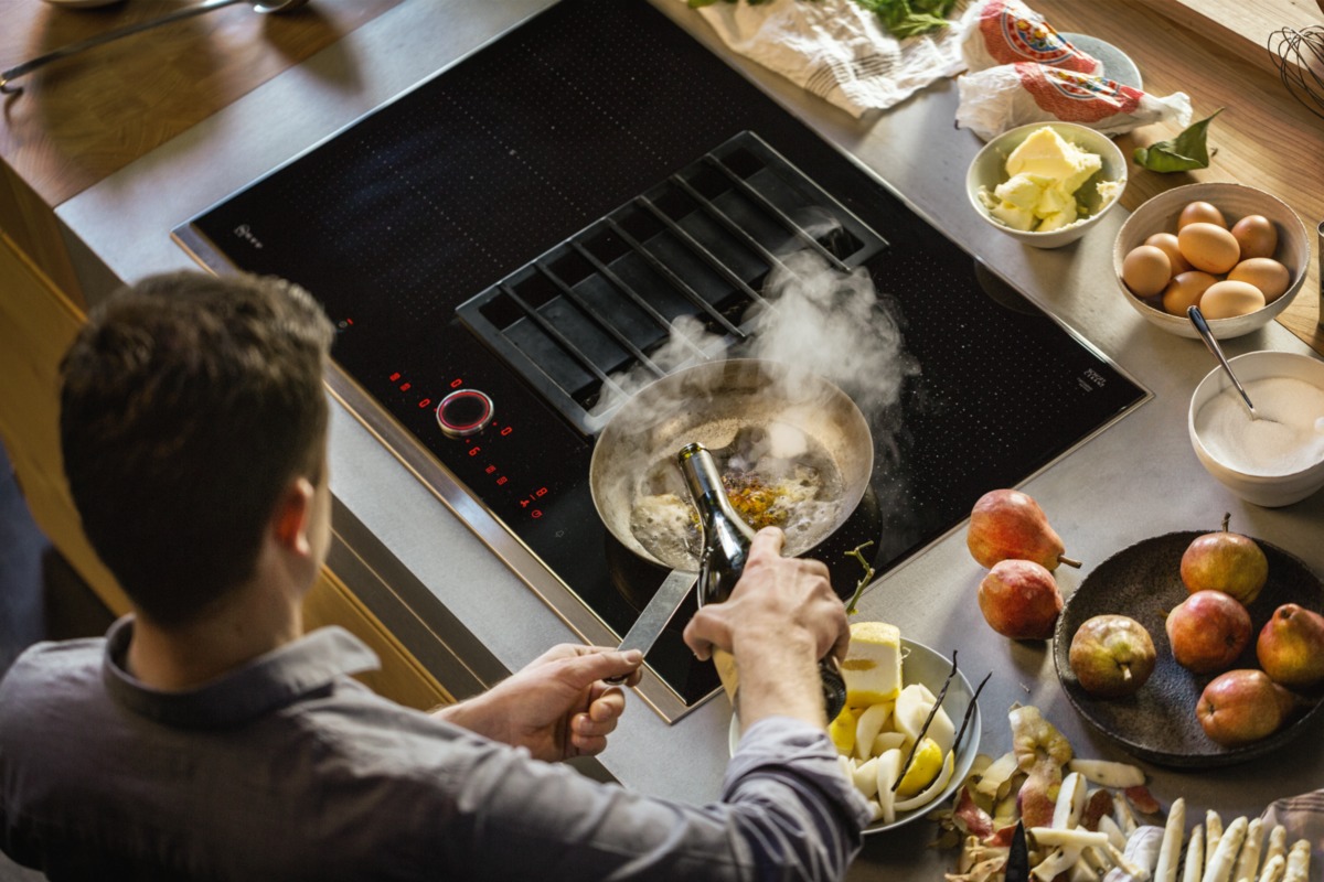 Person kocht auf Kochfeld mit integriertem Dunstabzug