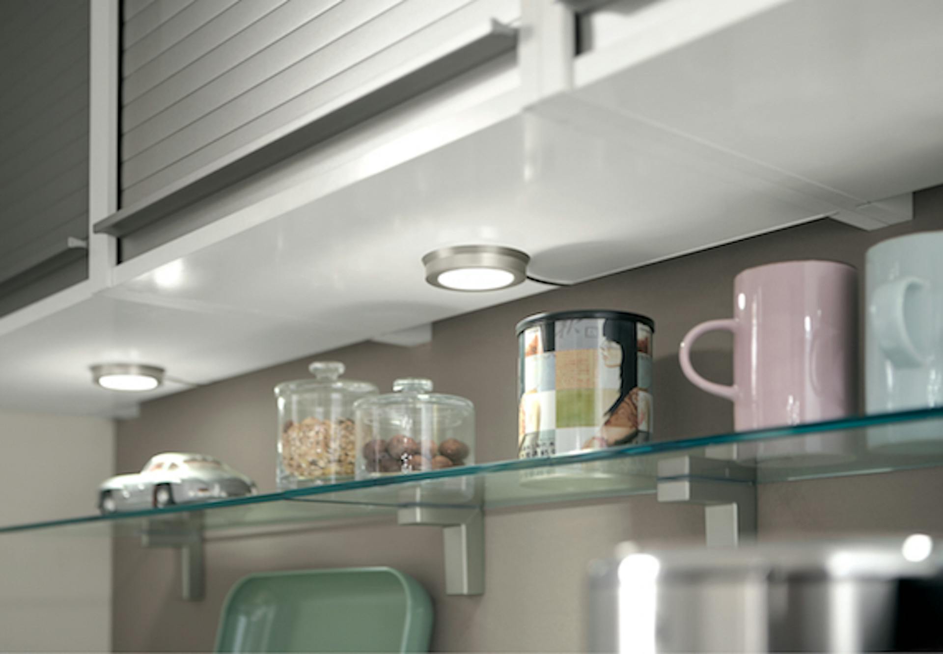 Luci sottopensili per la cucina sotto un pensile sopra uno scaffale con vasetti portaspezie e tazze.