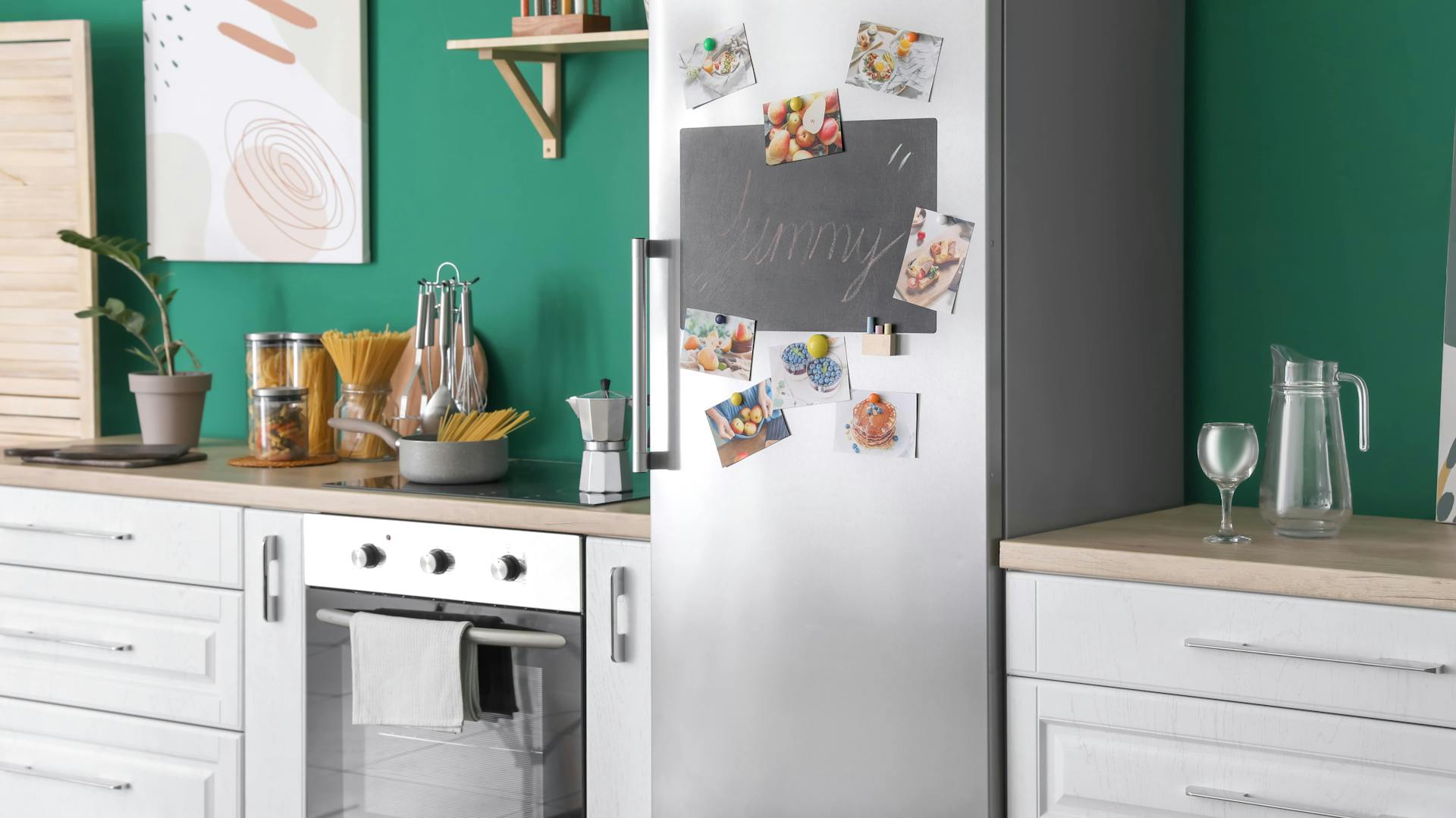 Helle Küchenzeile mit silbernem Kühlschrank vor grüner Wand.