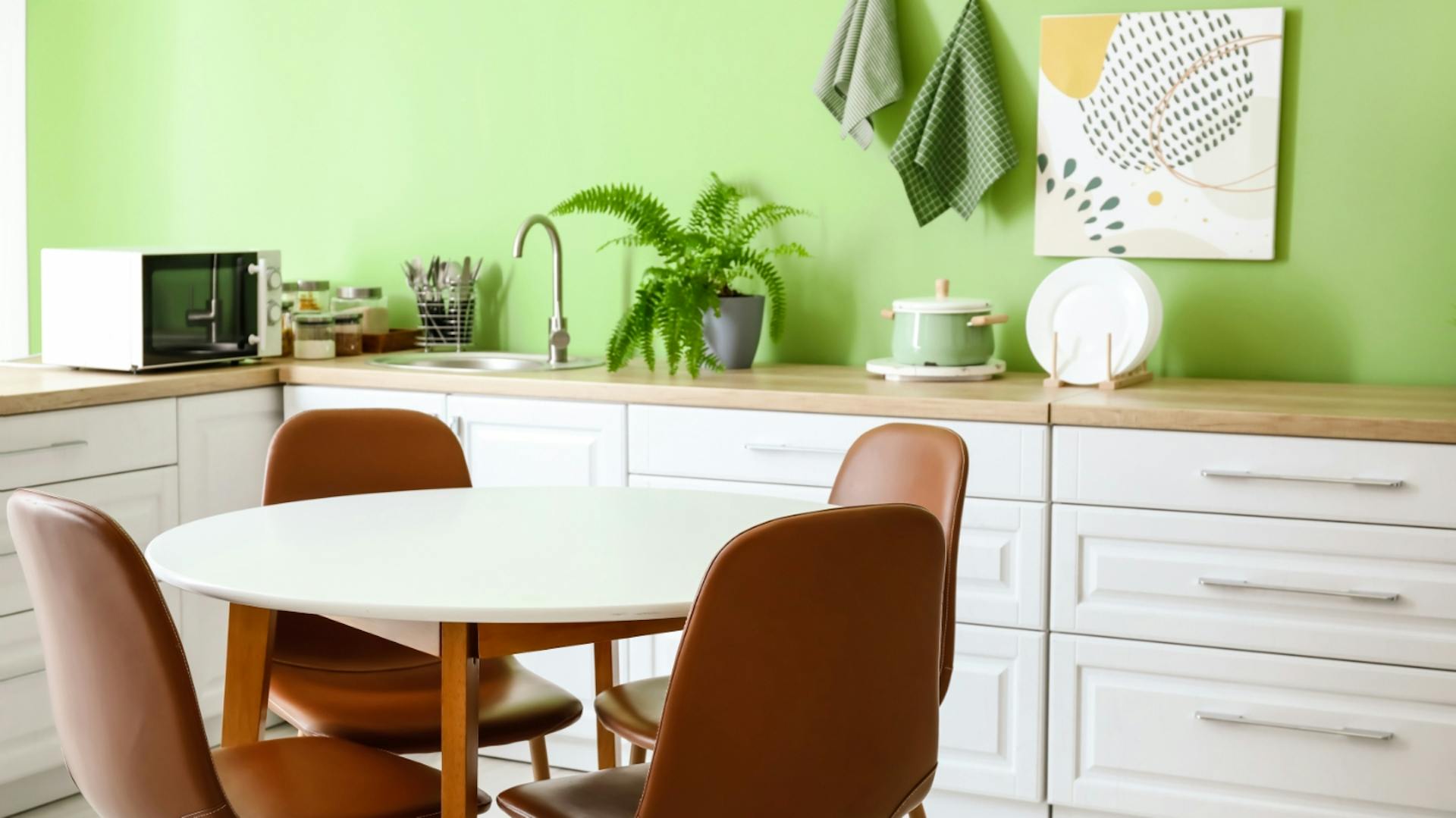 Weiße Küchenzeile vor einer hellgrünen Wand. Davor ein runder Tisch mit vier braunen Stühlen.
