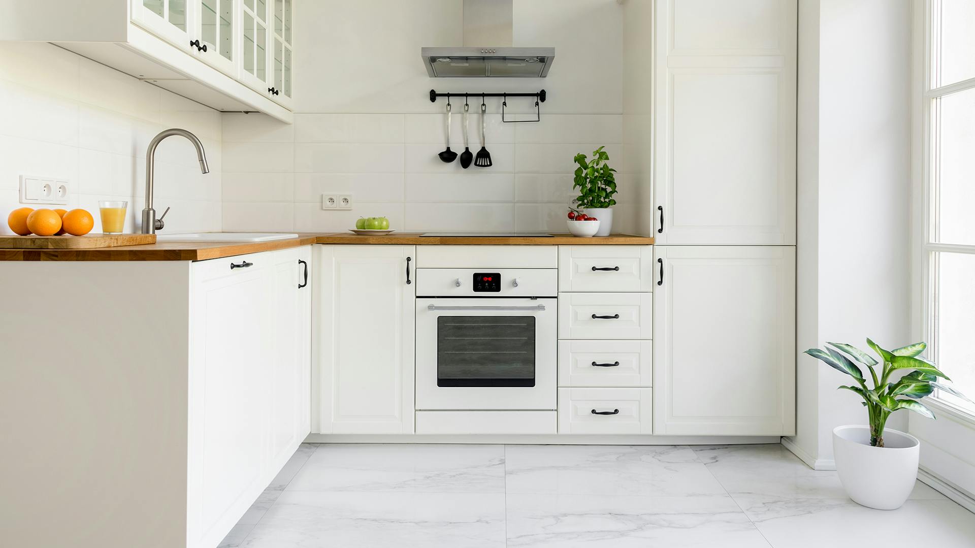 Moderne, weiße Küchenzeile mit hölzerner Arbeitsplatte vor weißer Wand.