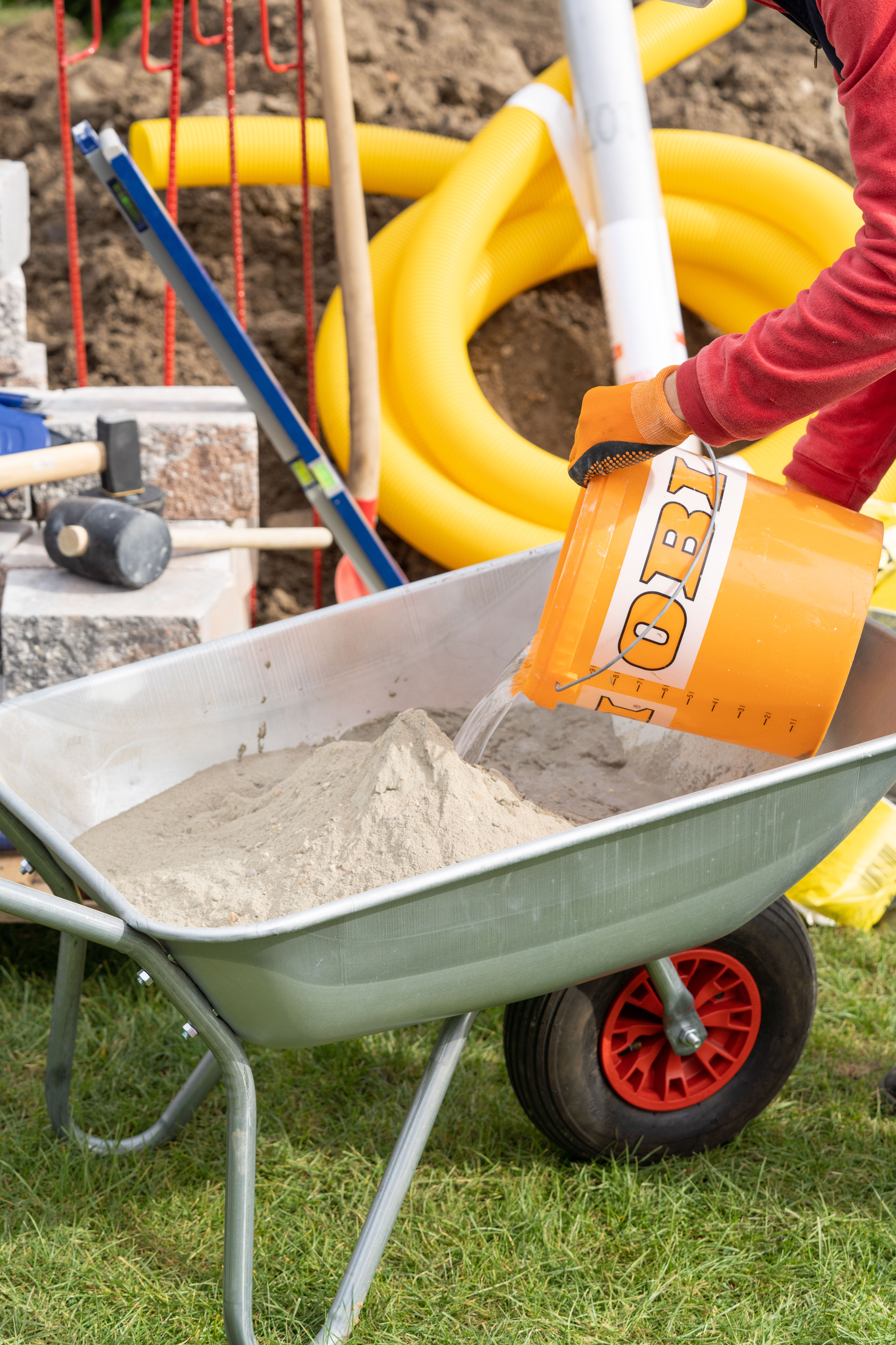 Un uomo versa l’acqua da un secchio in una carriola con malta