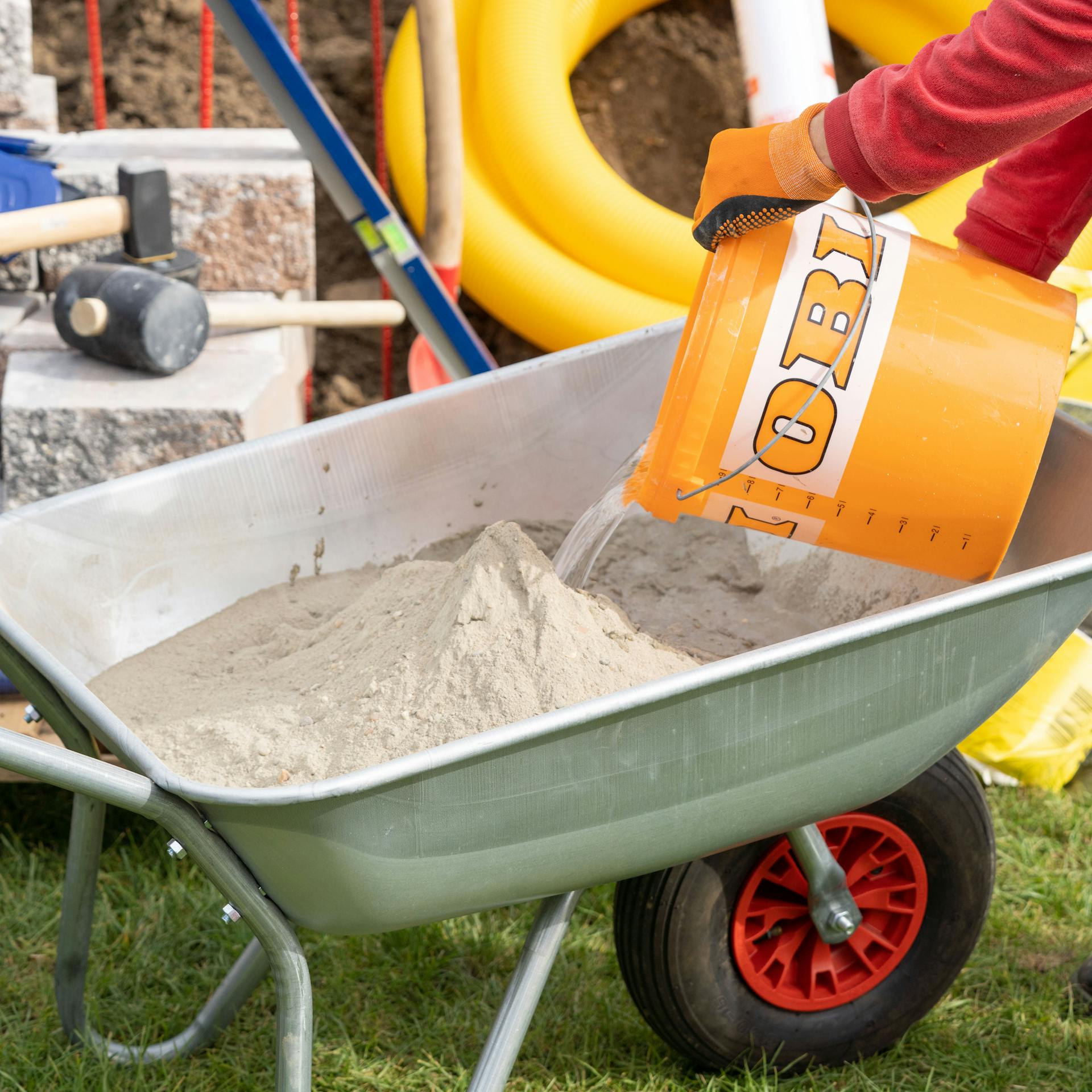 Mann schüttet Wasser aus einem Eimer in eine Schubkarre mit Mörtel