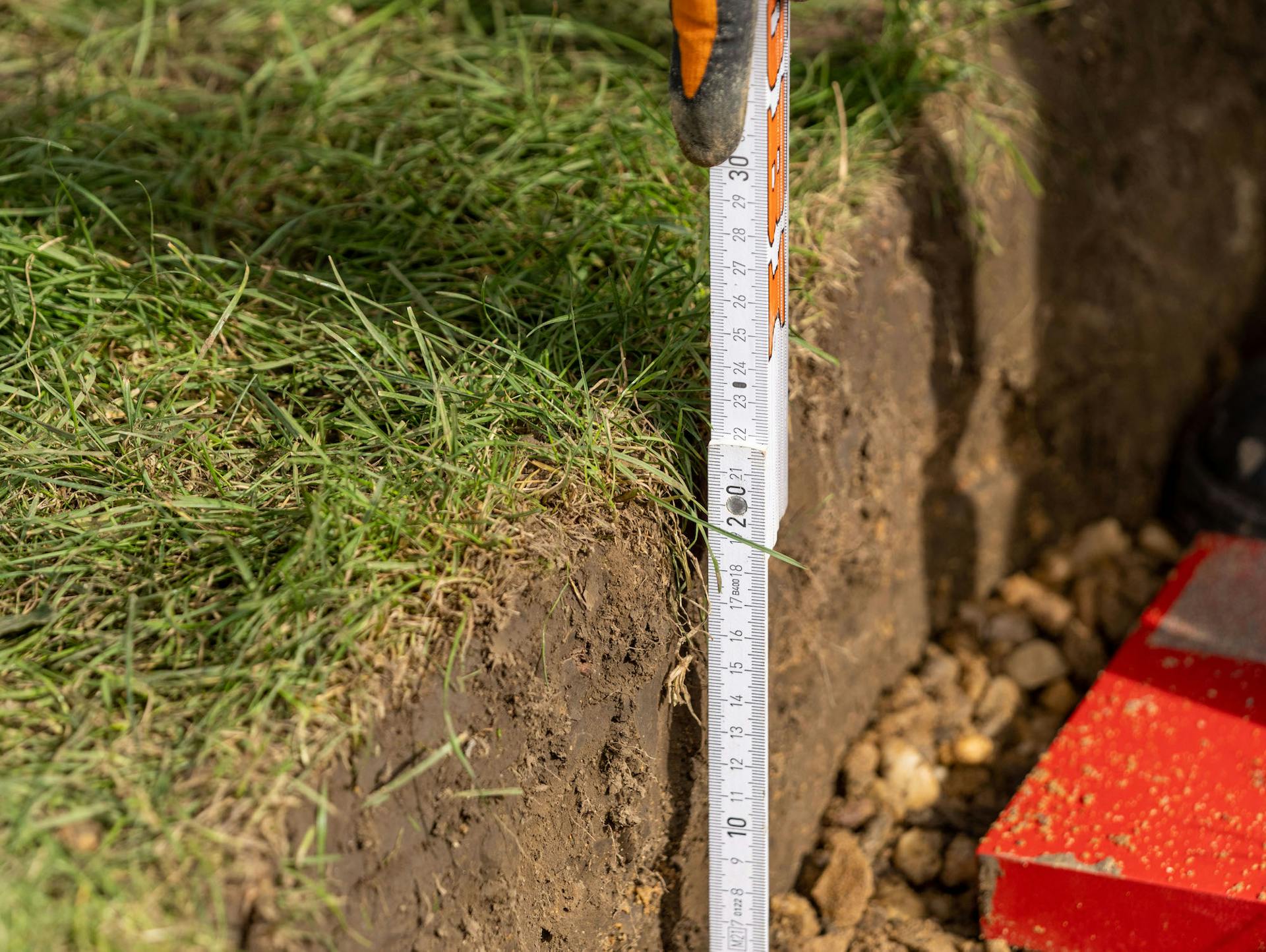 Heimwerker misst Aushub für Gartenhaus-Fundament mit Zollstock.