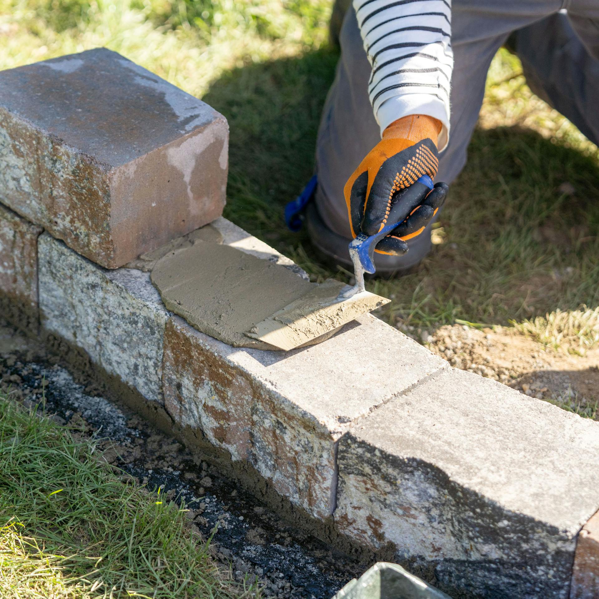 Person verteilt Mörtel auf Steinreihe