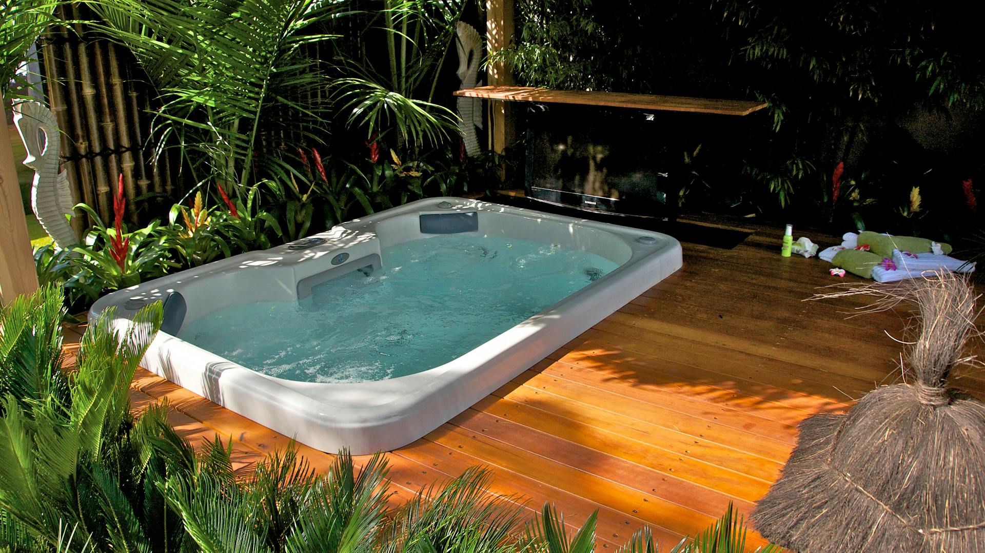 Whirlpool auf tropisch gestalteter Terrasse mit Holzboden und Pflanzen.