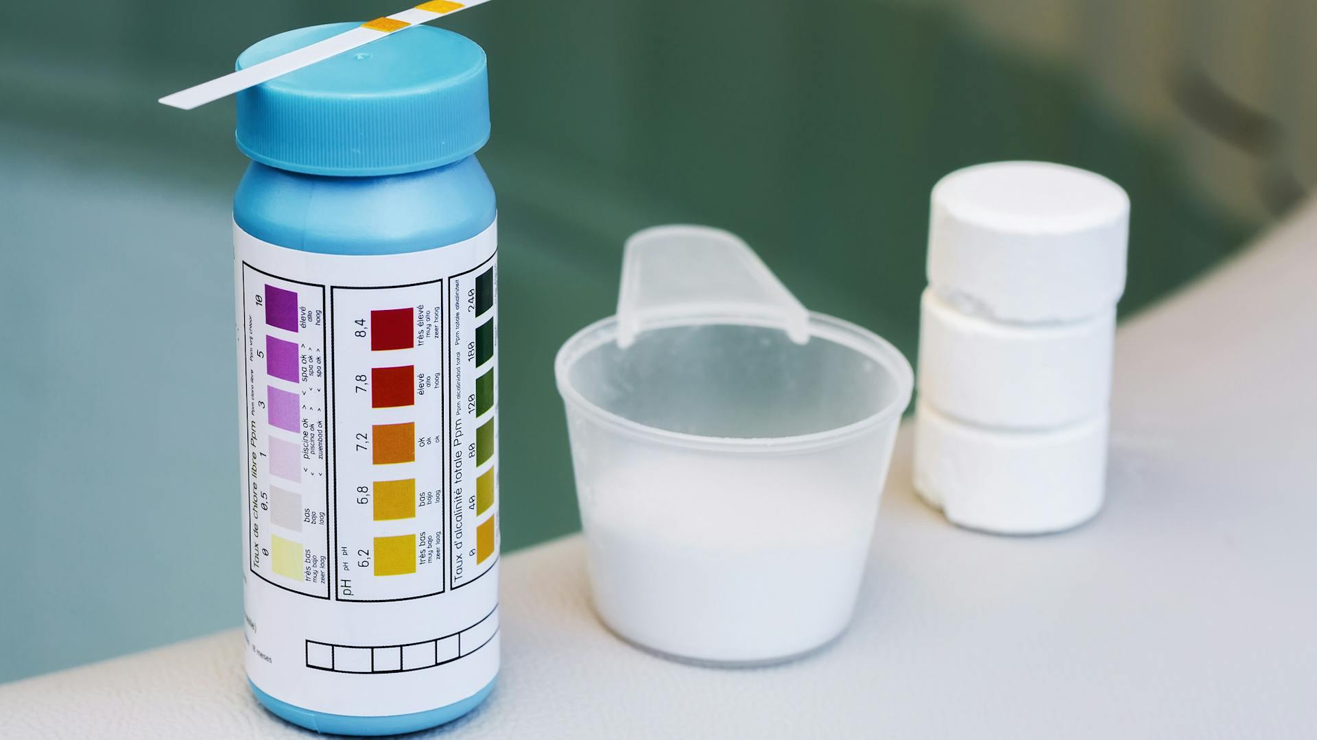 Teststreifen und Dosierlöffel am Rand eines Pools.