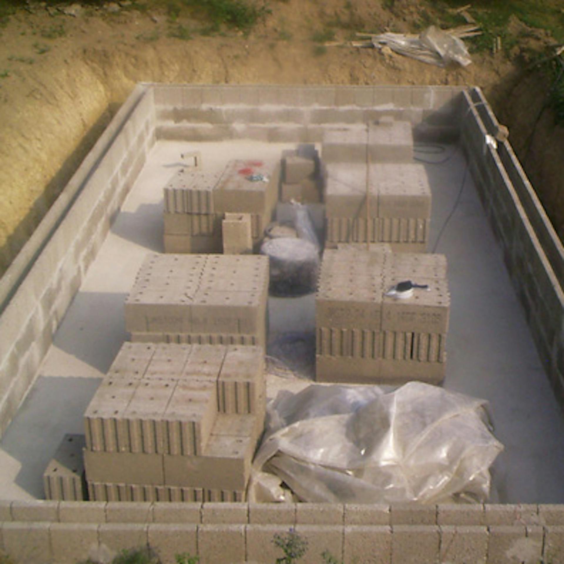 A medence falait már megépítették. A medencében téglák vannak.