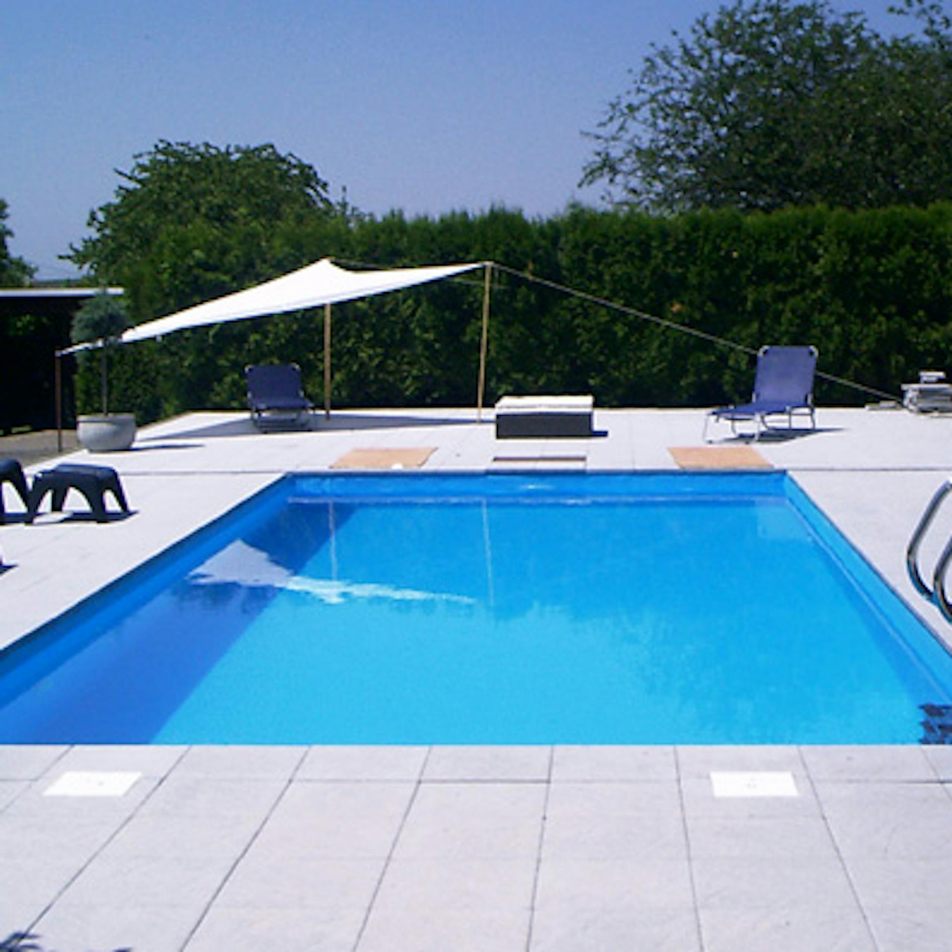 Kész medence létrával, nyugágyakkal és napernyővel.