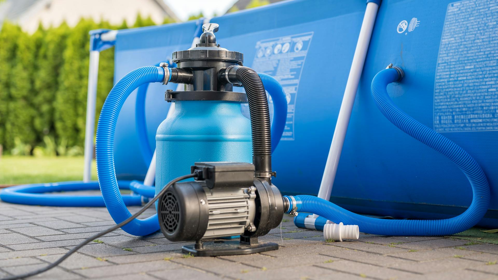 Un impianto di filtrazione a sabbia si trova di fronte a una piscina blu fuori terra.