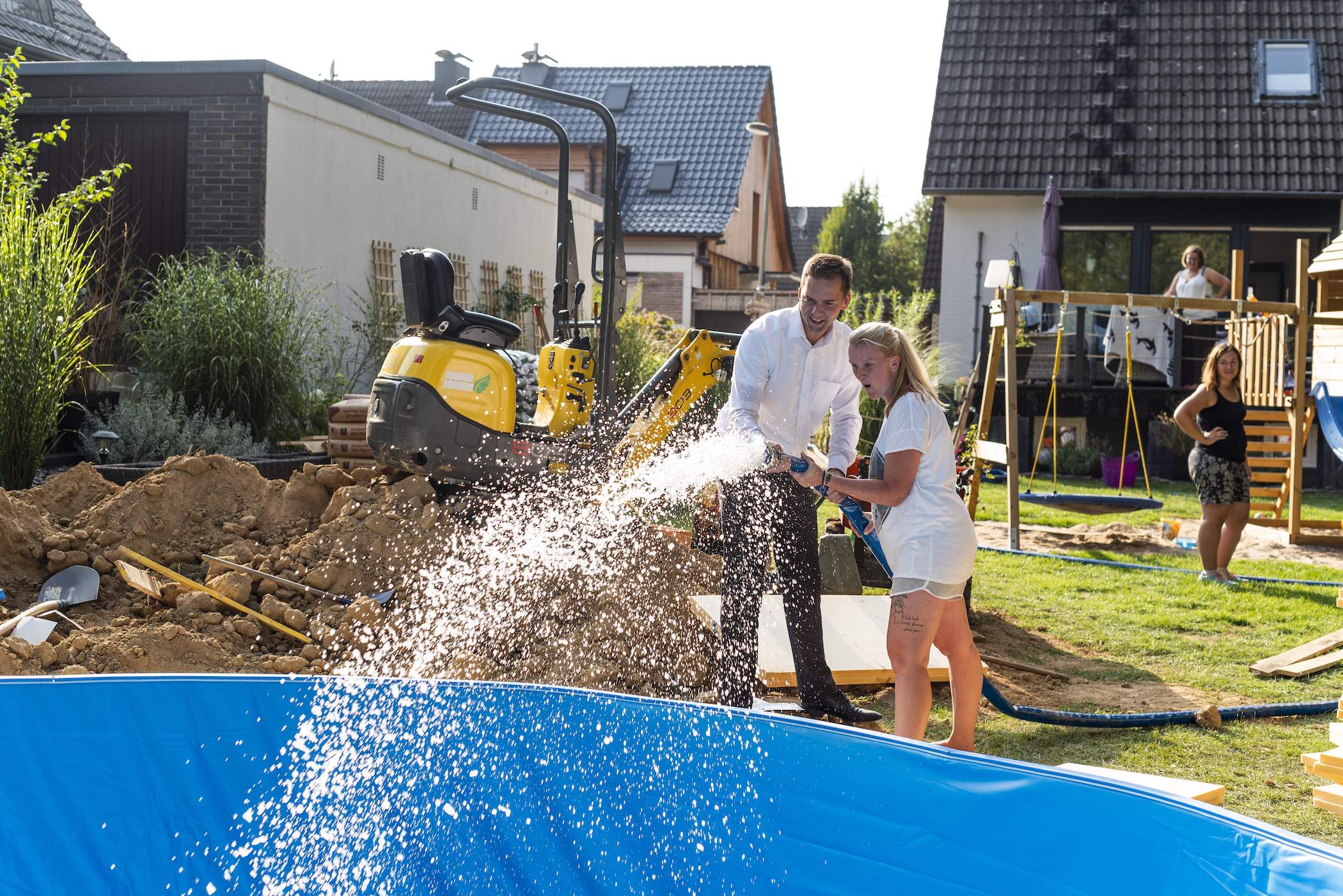 Zwei Personen füllen mit einem Schlauch Wasser in einen Pool.
