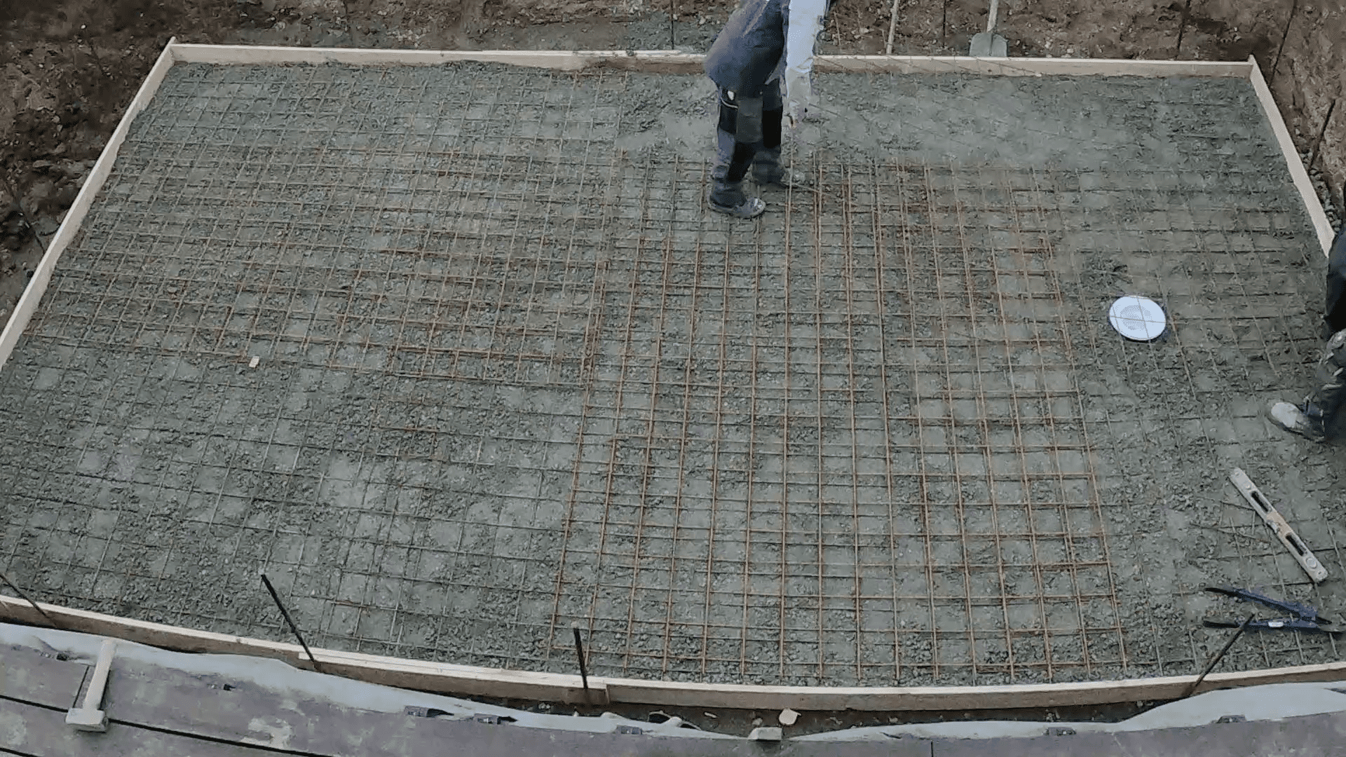 Heimwerker verteilt Beton in Bodenplatte mit Bewehrung.