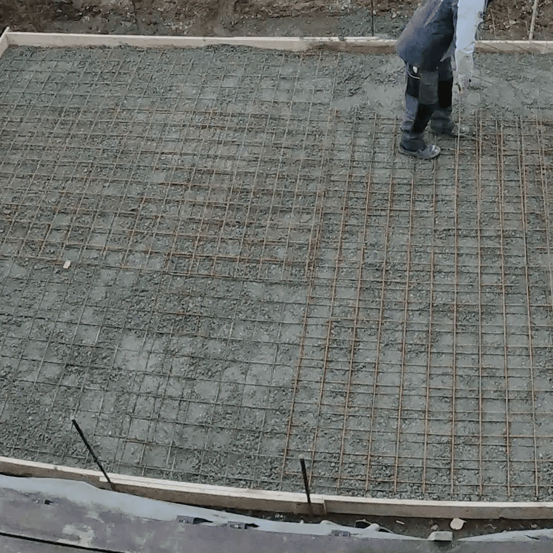Heimwerker verteilt Beton in Bodenplatte mit Bewehrung.