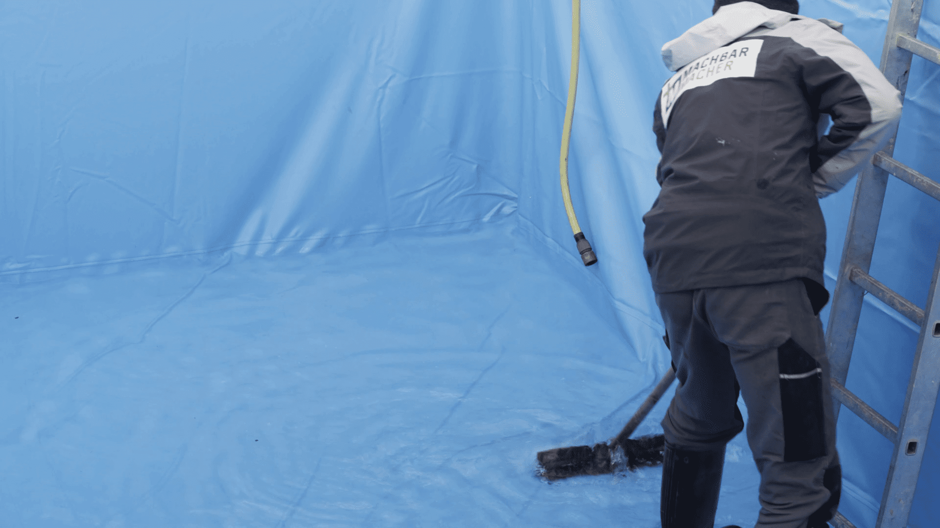 Heimwerker glättet Poolfolie am Boden mit Besen.