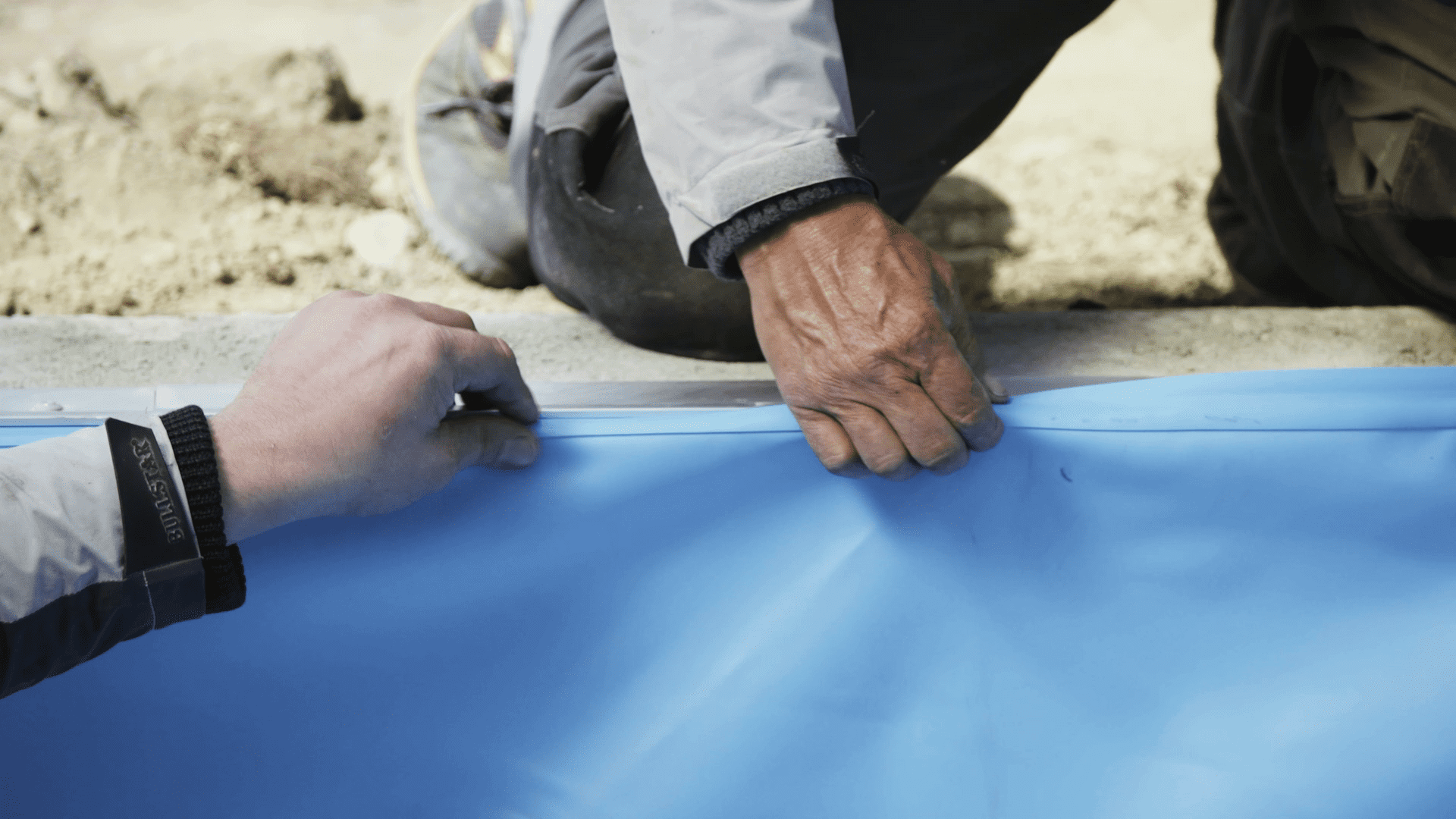 Heimwerker befestigen Poolfolie an Beckenwand.