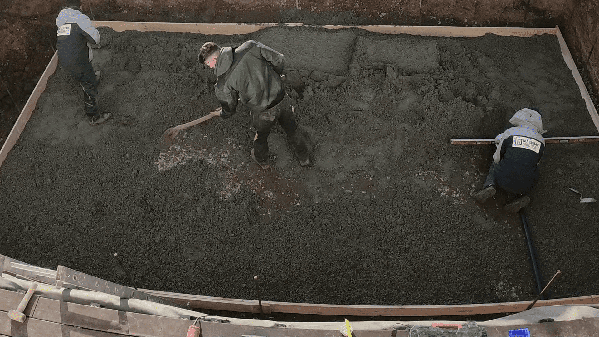 Heimwerker verteilen eingefüllten Schotter in Baugrube mit Schaufel.