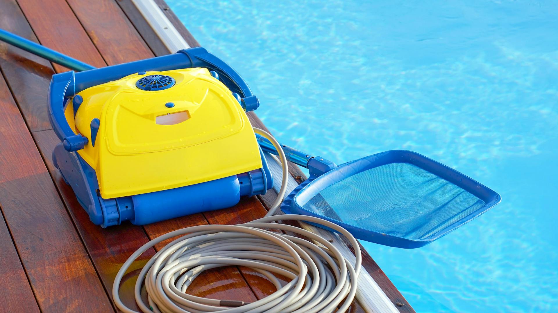 Blau-gelber Poolroboter mit Kabel und Kescher am Poolrand