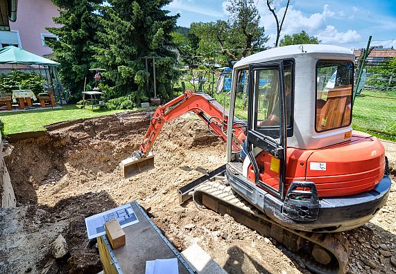 Bagger hebt Grube für Schwimmteich im Garten aus.