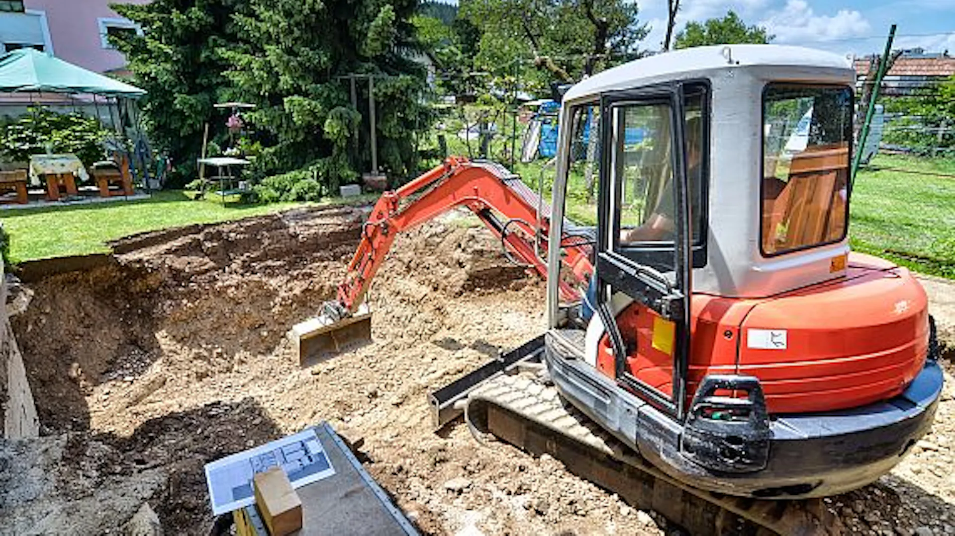 Bagger hebt Grube für Schwimmteich im Garten aus.