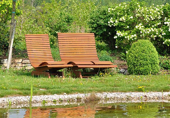 Braune Gartenbänke stehen am Ufer des Schwimmteichs.