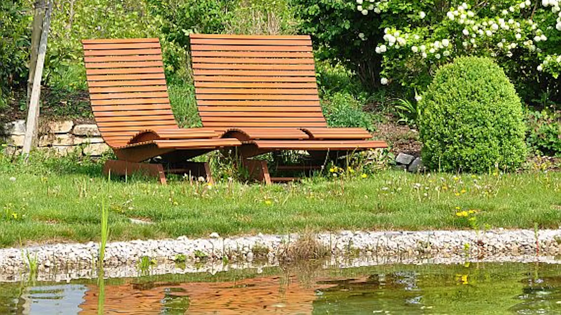 Braune Gartenbänke stehen am Ufer des Schwimmteichs.