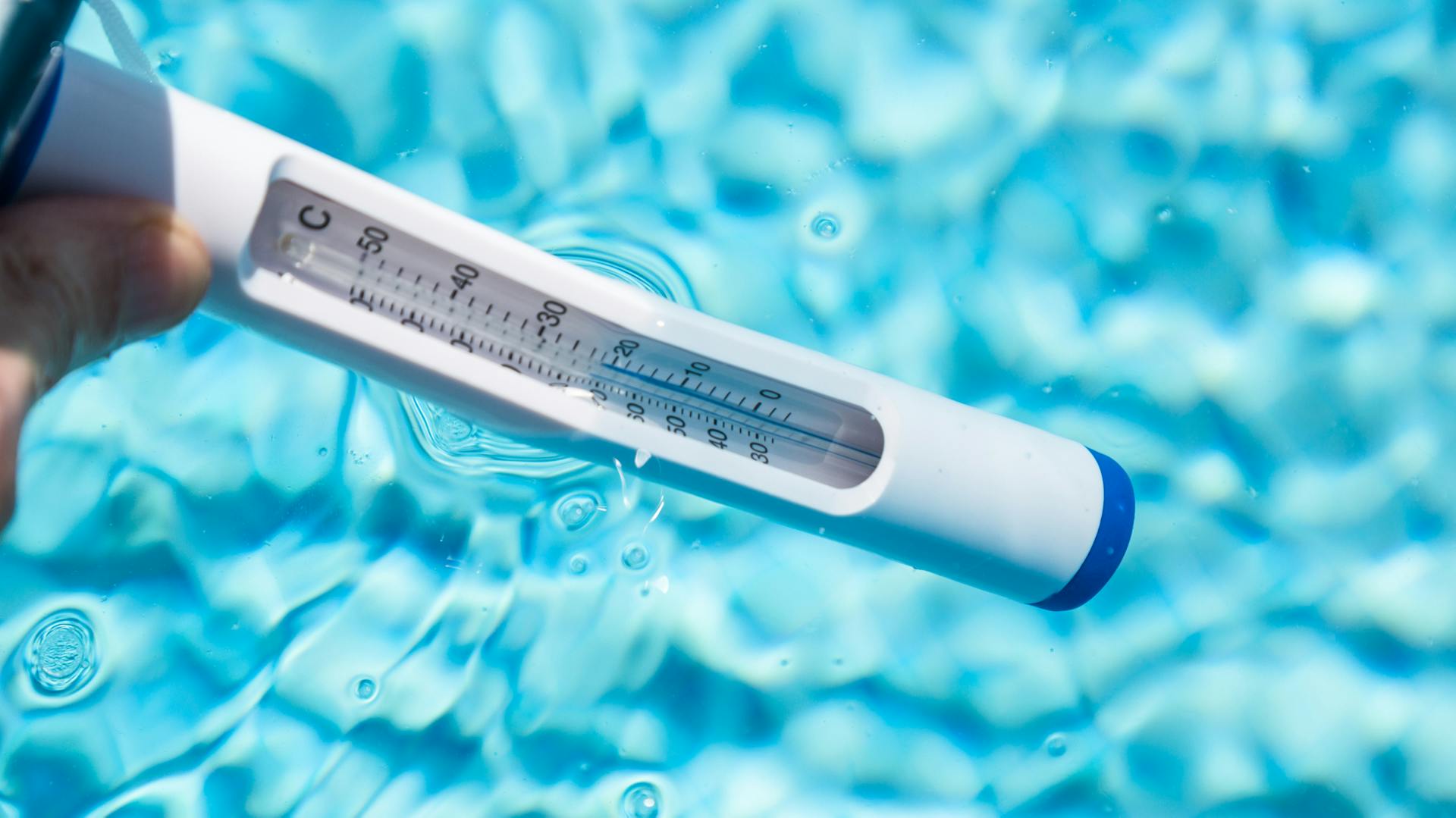Eine Person hält ein Thermometer ins Poolwasser.
