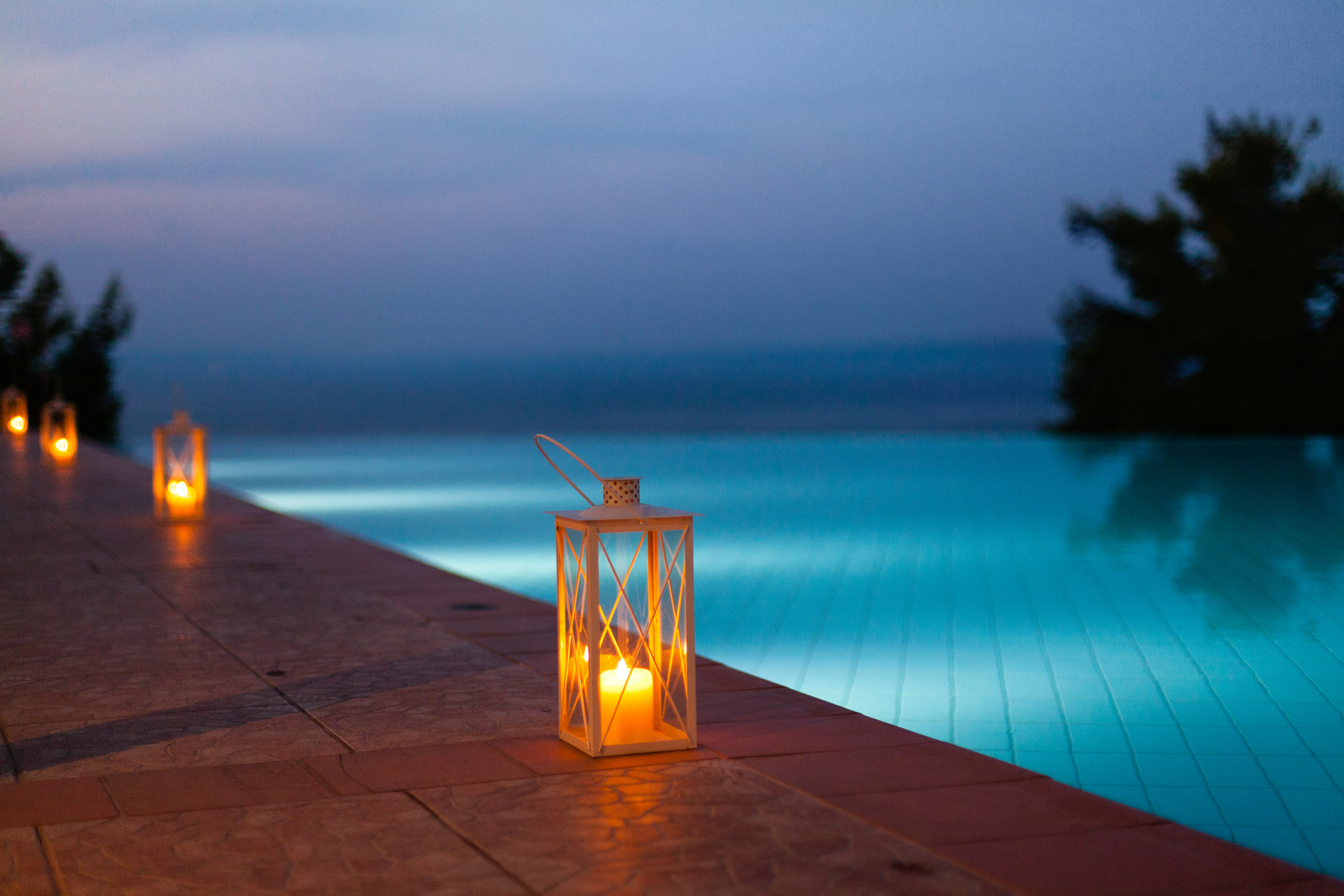 Pool am Abend mit Poolumrandung aus Stein und Laternen am Beckenrand