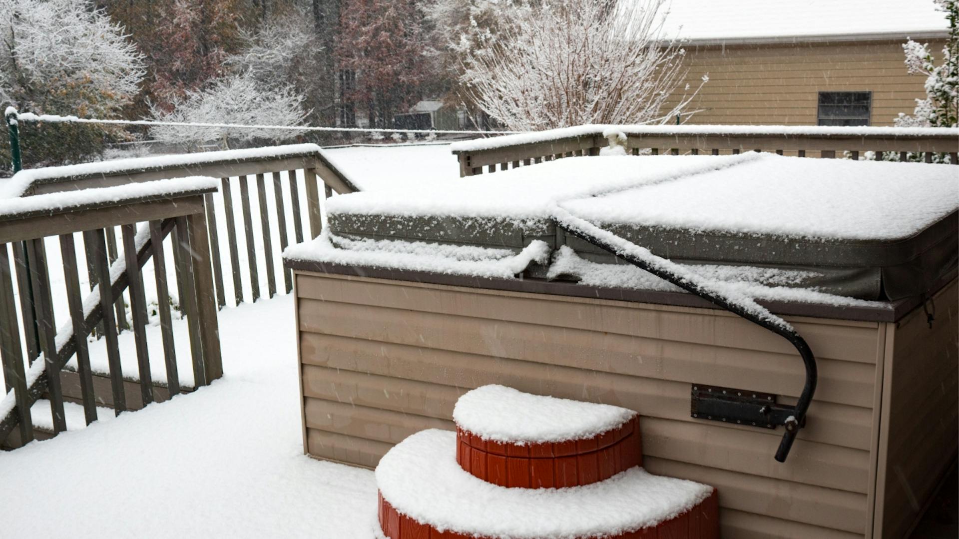 Schneebedeckter Whirlpool mit Treppe und Abdeckung steht auf Terrasse.