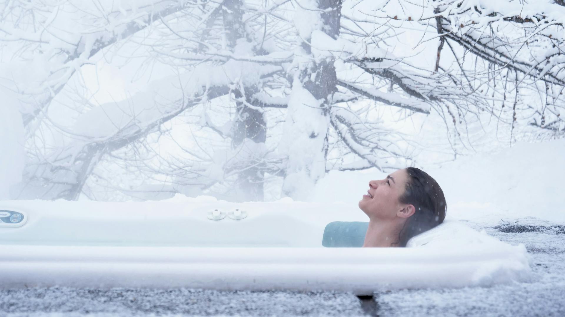 Frau badet in schneebedecktem Whirlpool am Waldrand.