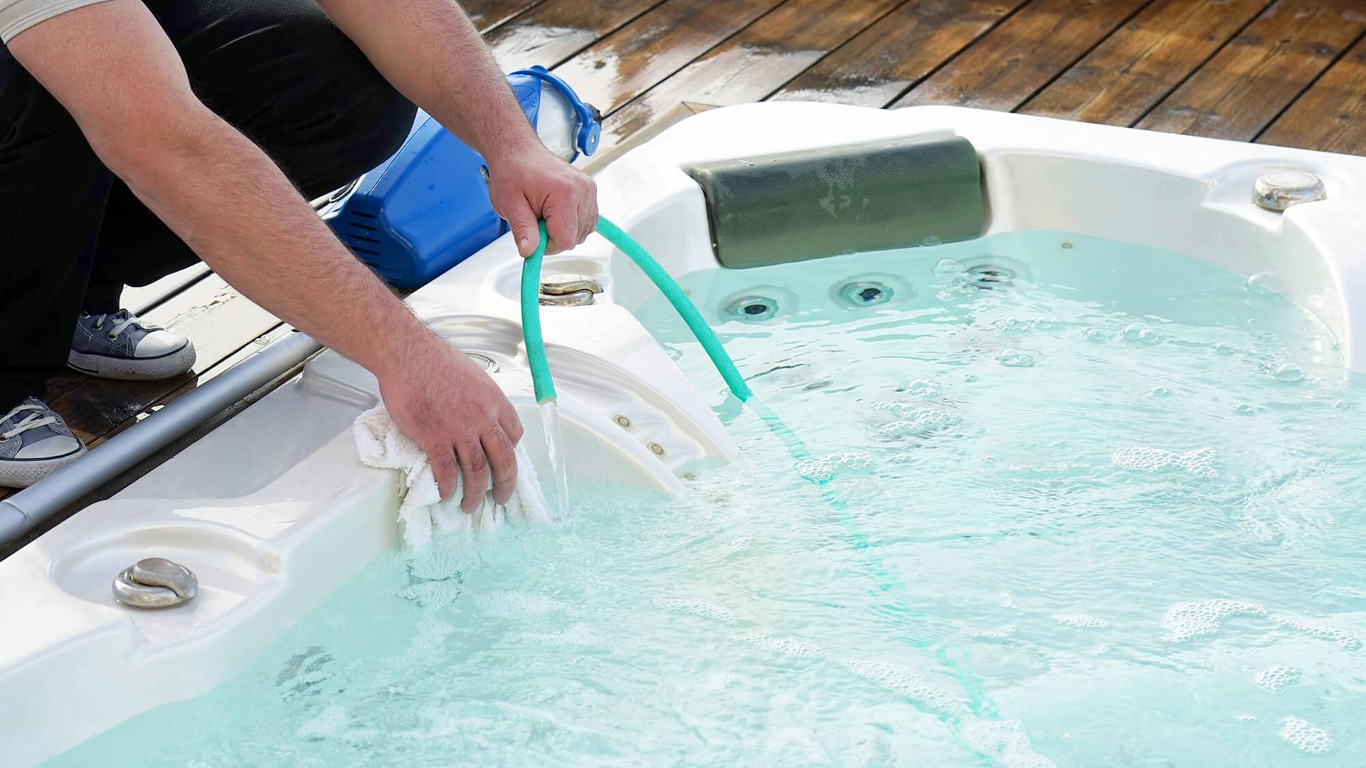 Person reinigt Whirlpool mit Wasserschlauch und Putzlappen