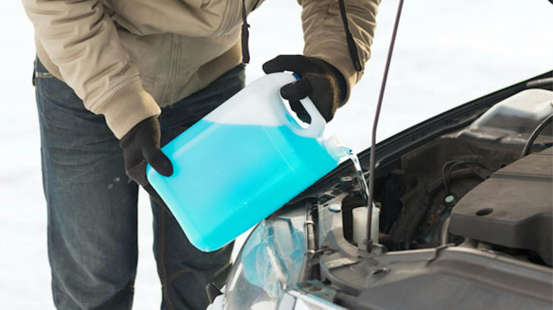 Mann füllt Scheibenfrostschutz unter Motorhaube ein.