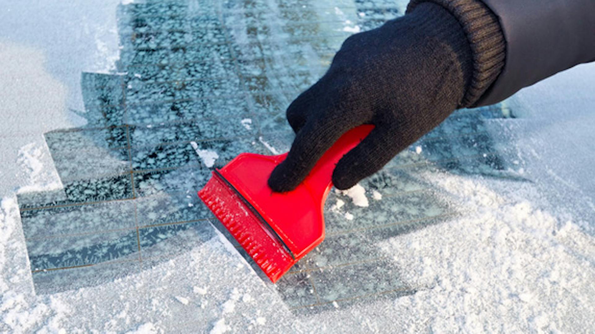 Hand mit Eiskratzer auf vereister Frontscheibe.