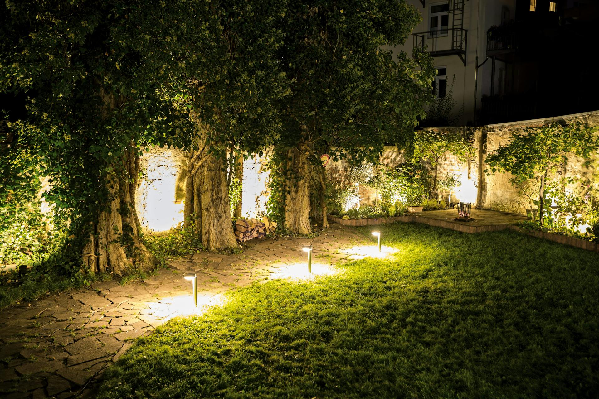 Lampade da terra in giardino con prato, selciato, alberi e muri di notte