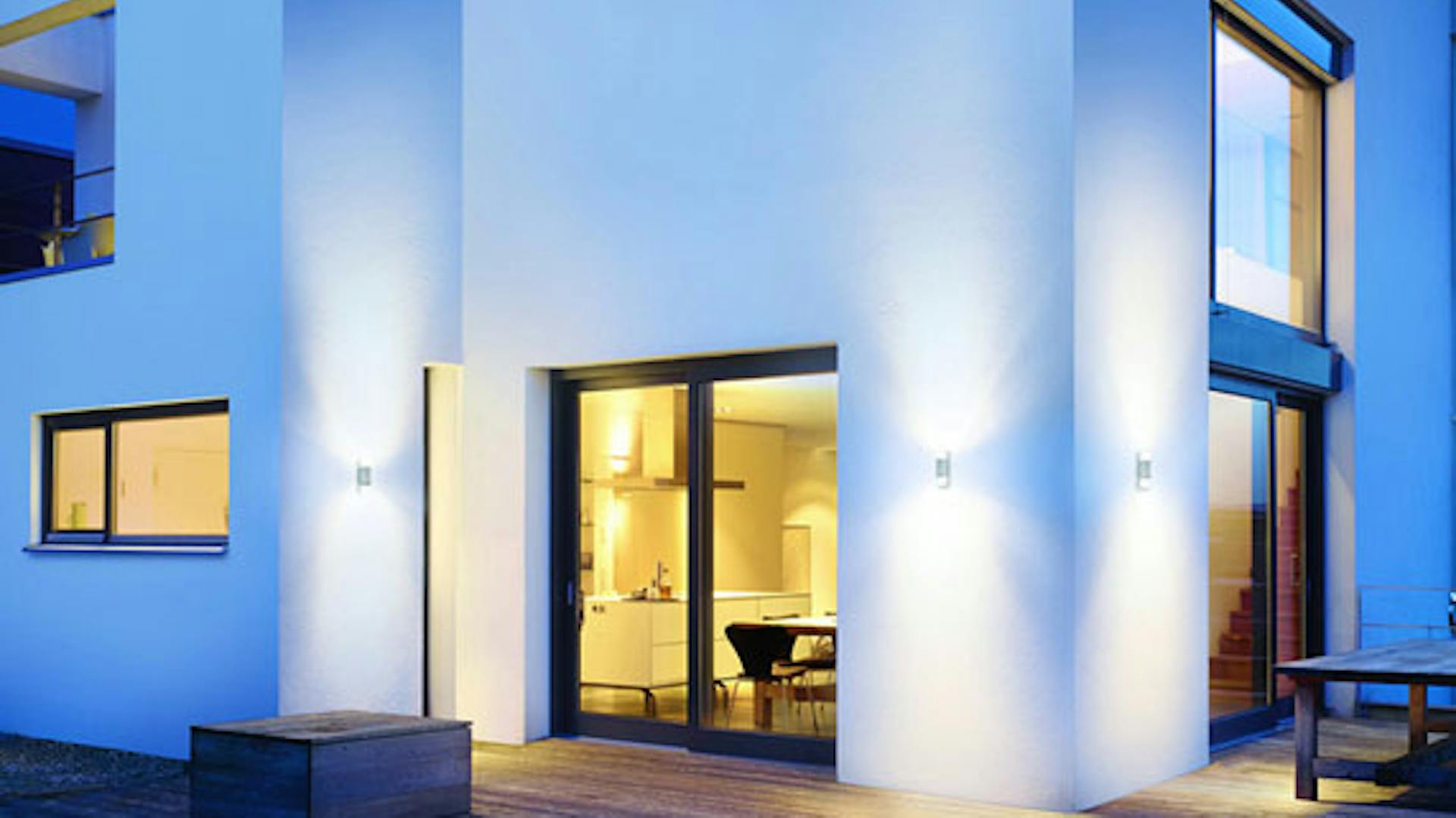 Außenbeleuchtung in der Dämmerung an modernem Gebäude mit weißer Fassade und großen Fenstern