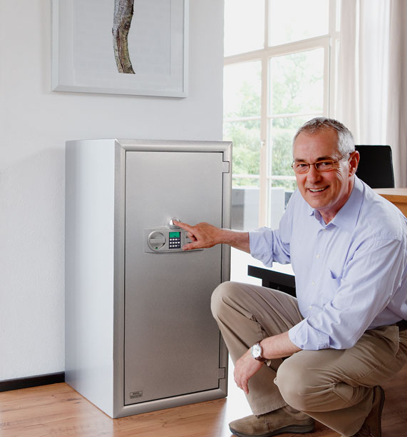 Mann kniet mit Finger auf dem Eingabefeld vor Tresor