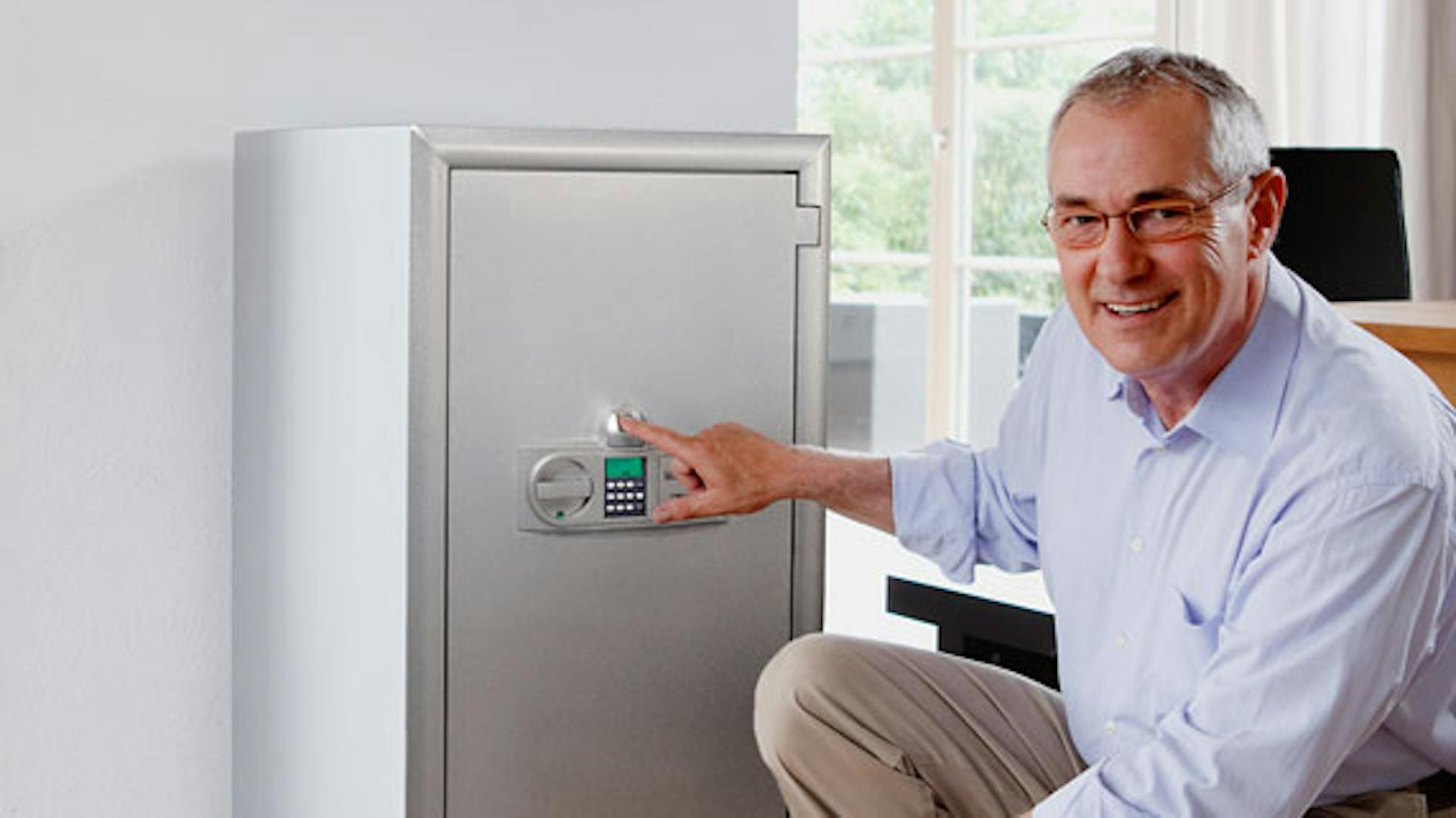 Mann kniet mit Finger auf dem Eingabefeld vor Tresor